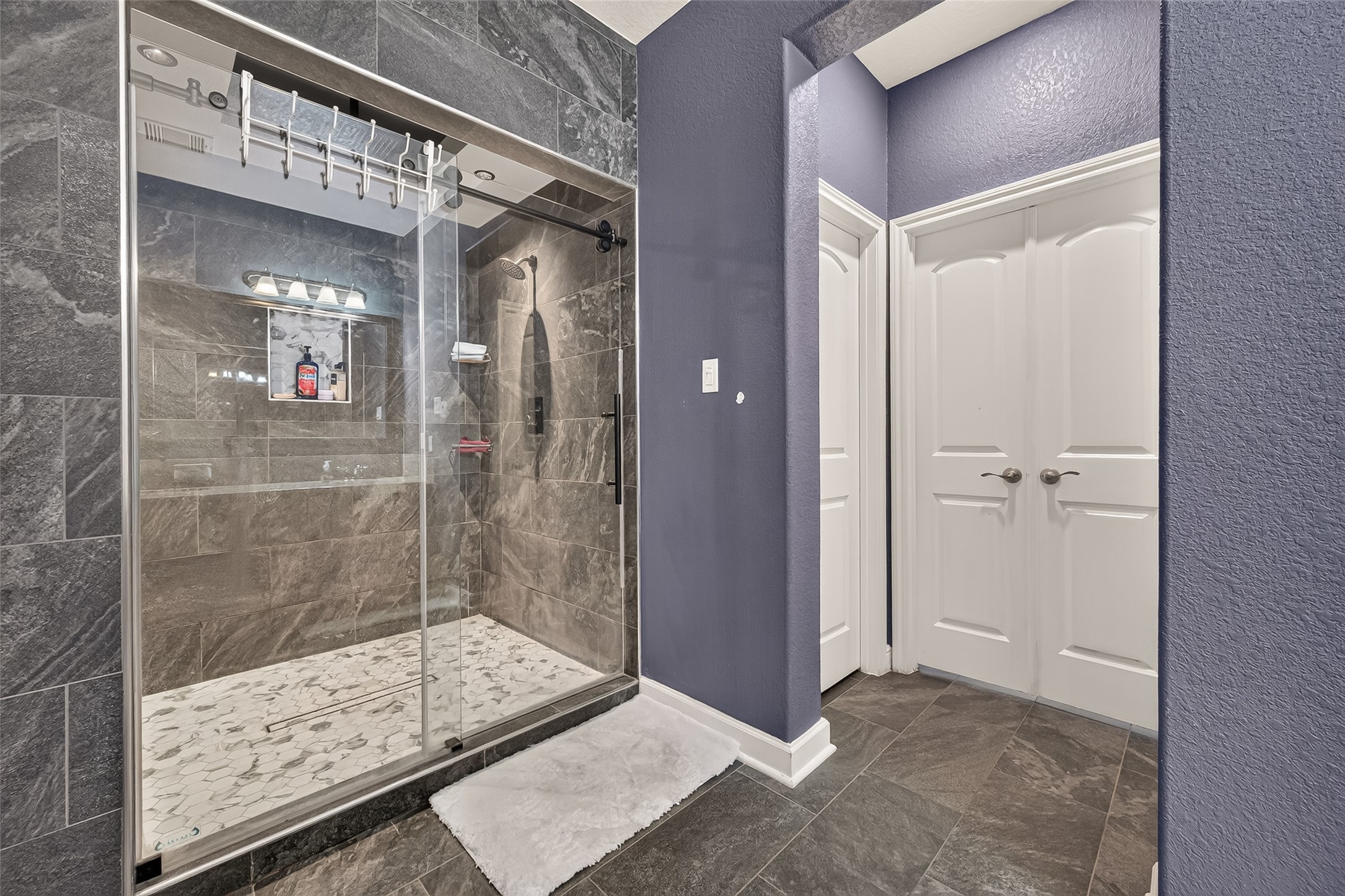 Refined primary bathroom featuring a spacious glass-enclosed shower with sleek dark tilework and contemporary fixtures, complemented by elegant double doors opening to an expansive walk-in closet.