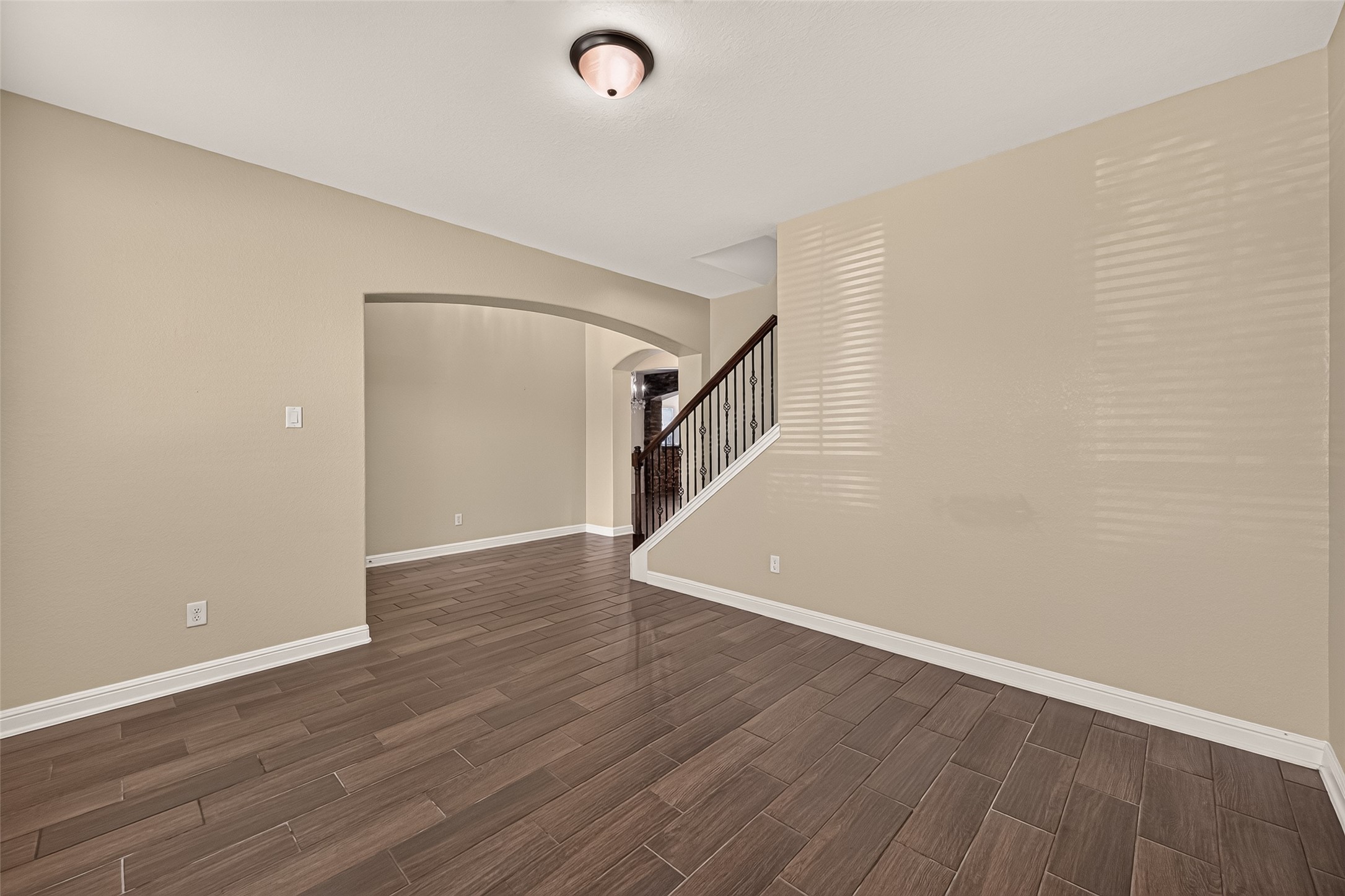Spacious Office area with elegant wood-look tile flooring and a graceful archway leading to the staircase, creating a warm and inviting ambiance.