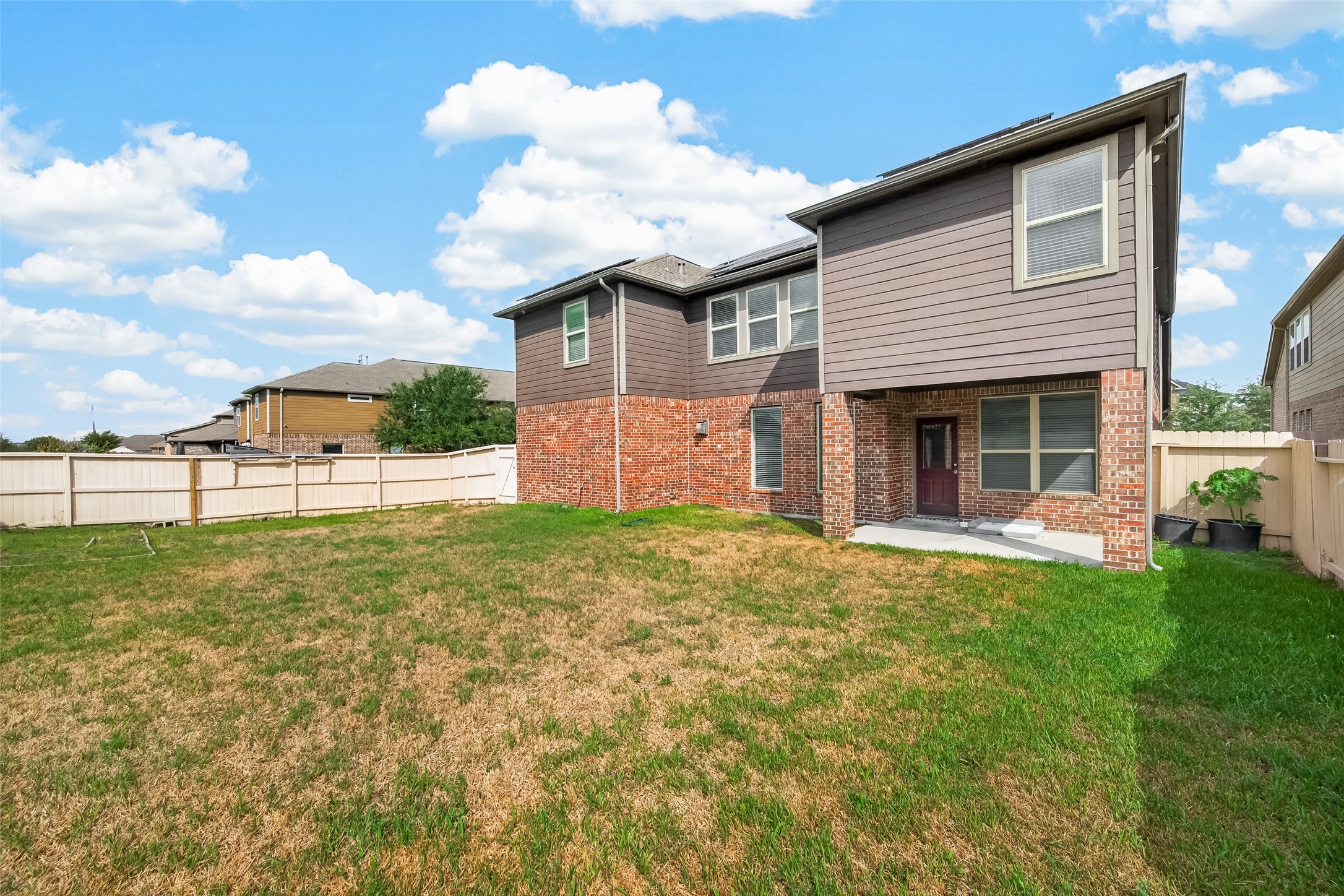 Spacious backyard with lush grass, perfect for outdoor activities, complemented by a two-story brick and siding home offering ample natural light and privacy with a fenced perimeter.
