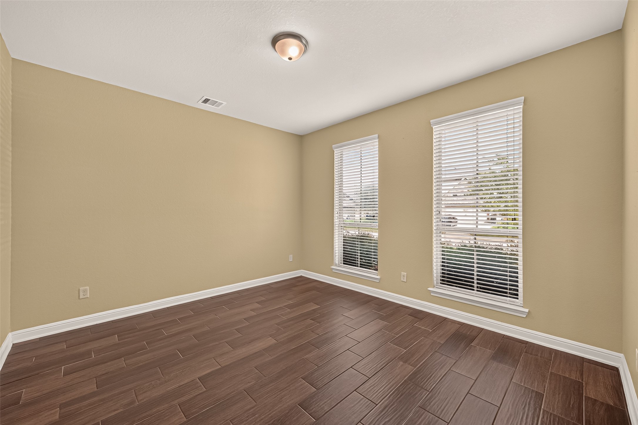 Bright office featuring elegant wood-look tile flooring and abundant natural light from two large windows with blinds.