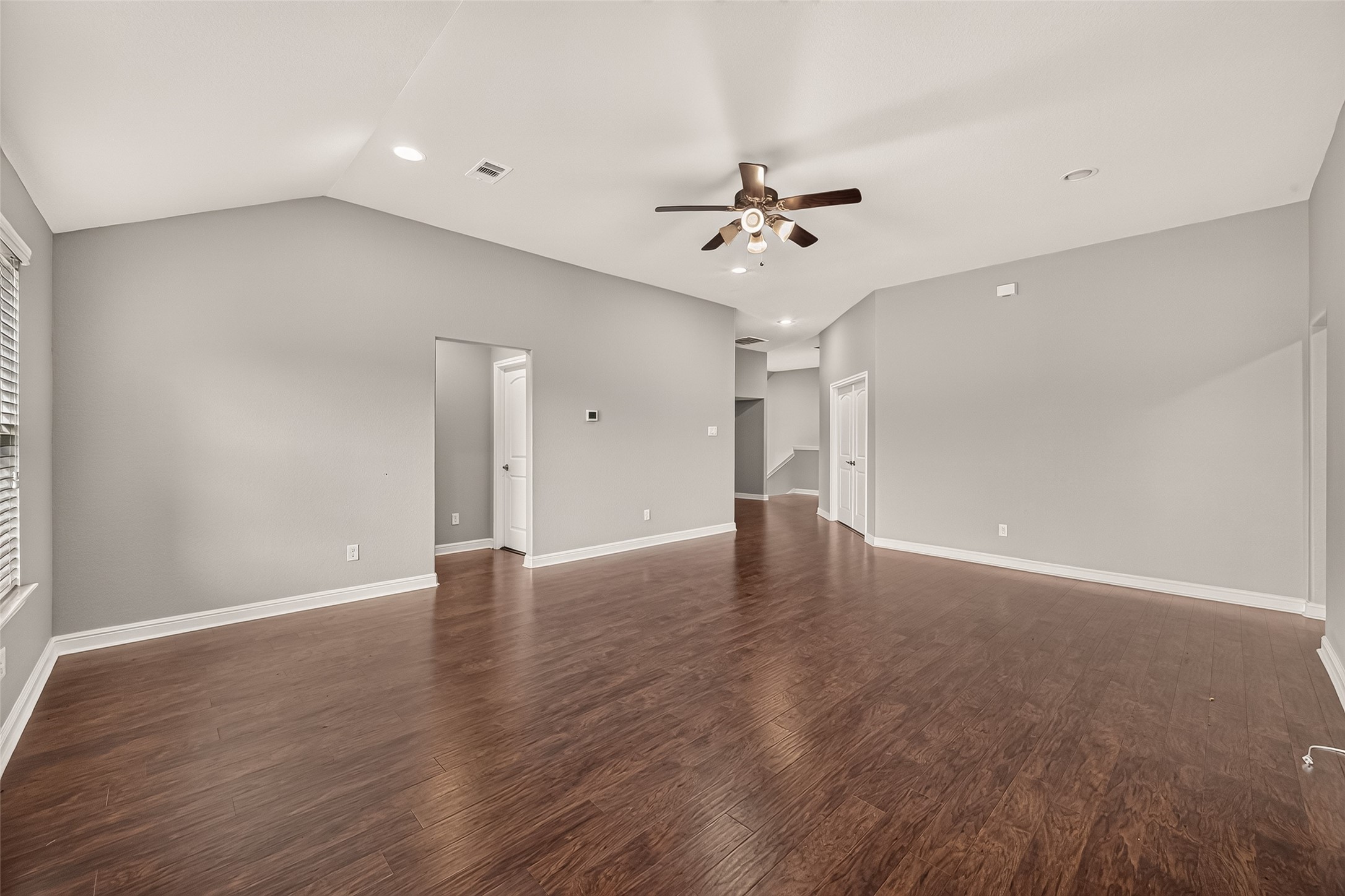 Spacious Game room area with elegant hardwood floors, ample natural light from large windows, and a modern ceiling fan, perfect for family gatherings.