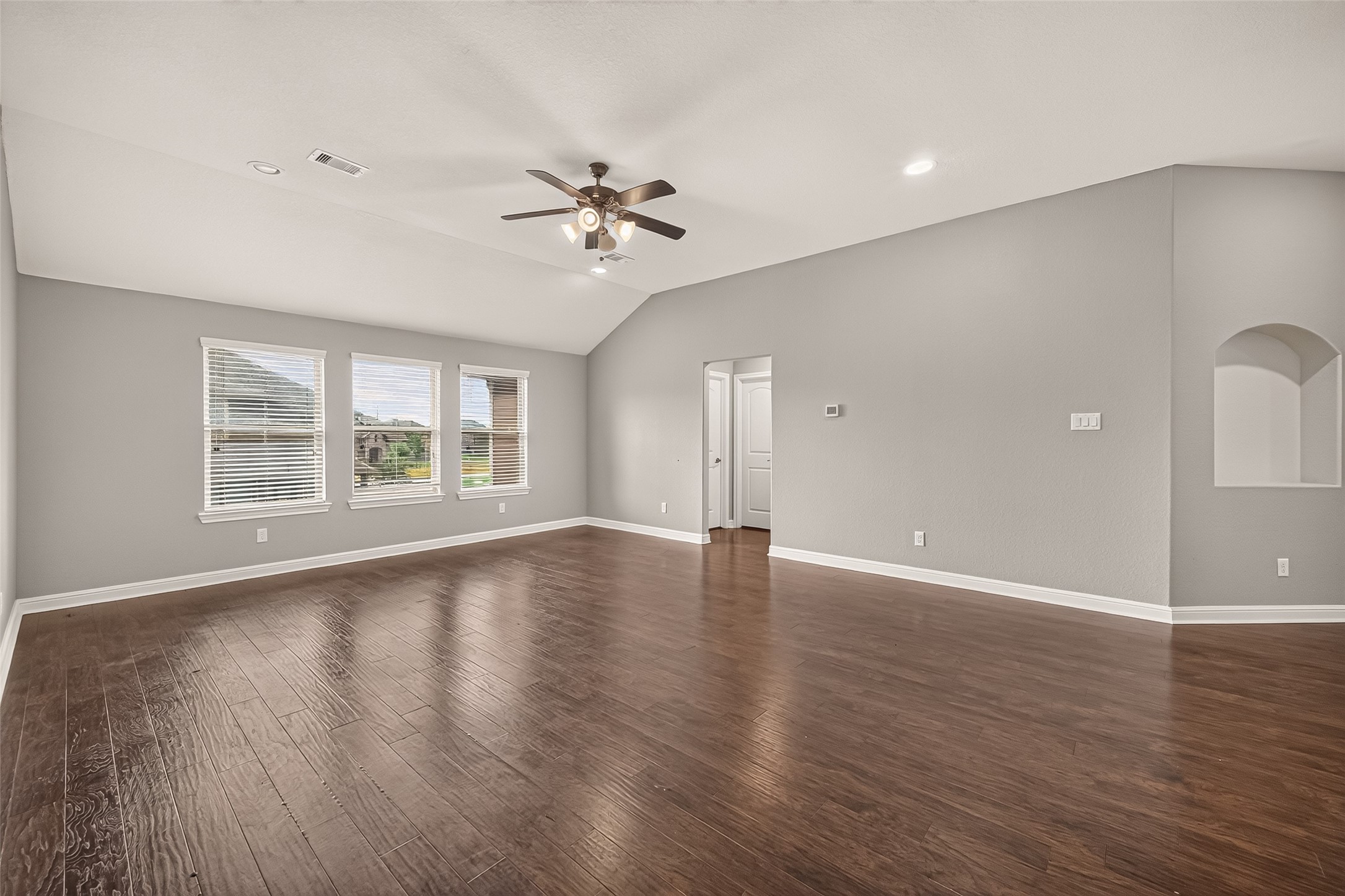Spacious Gameroom with elegant hardwood floors, ample natural light from large windows, and a modern ceiling fan, perfect for family gatherings.