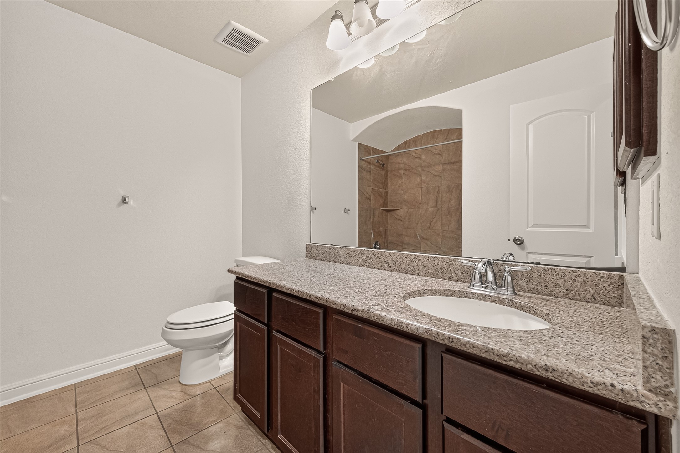 Spacious secondary bathroom featuring an expansive granite vanity with a porcelain sink, rich dark-wood cabinetry, and a stylish tiled shower.