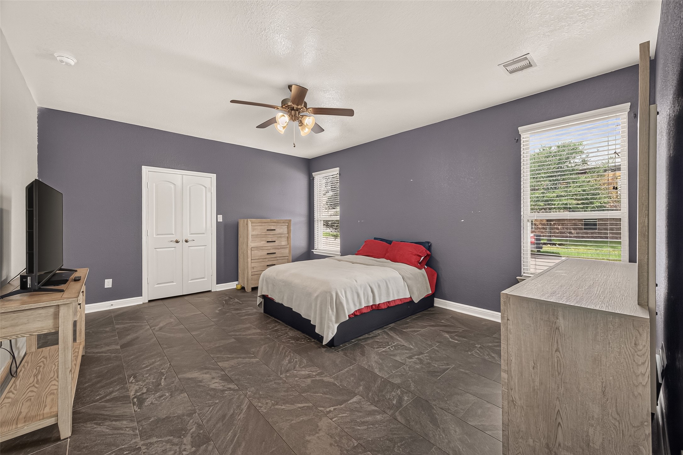 Luxurious primary suite showcasing sleek tile flooring, a contemporary ceiling fan, and expansive windows that bathe the space in natural light, creating a serene private retreat.