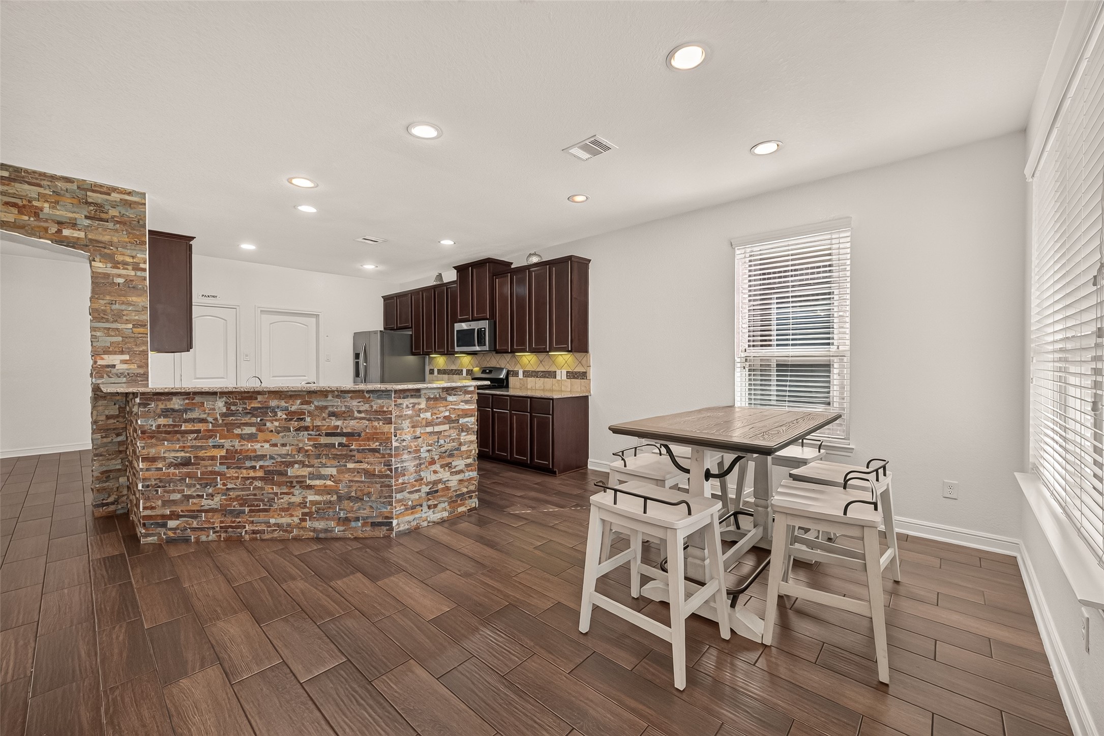 Spacious kitchen and breakfast area with rich dark-wood cabinetry, a stylish stone accent wall, and a cozy, light-filled dining nook.