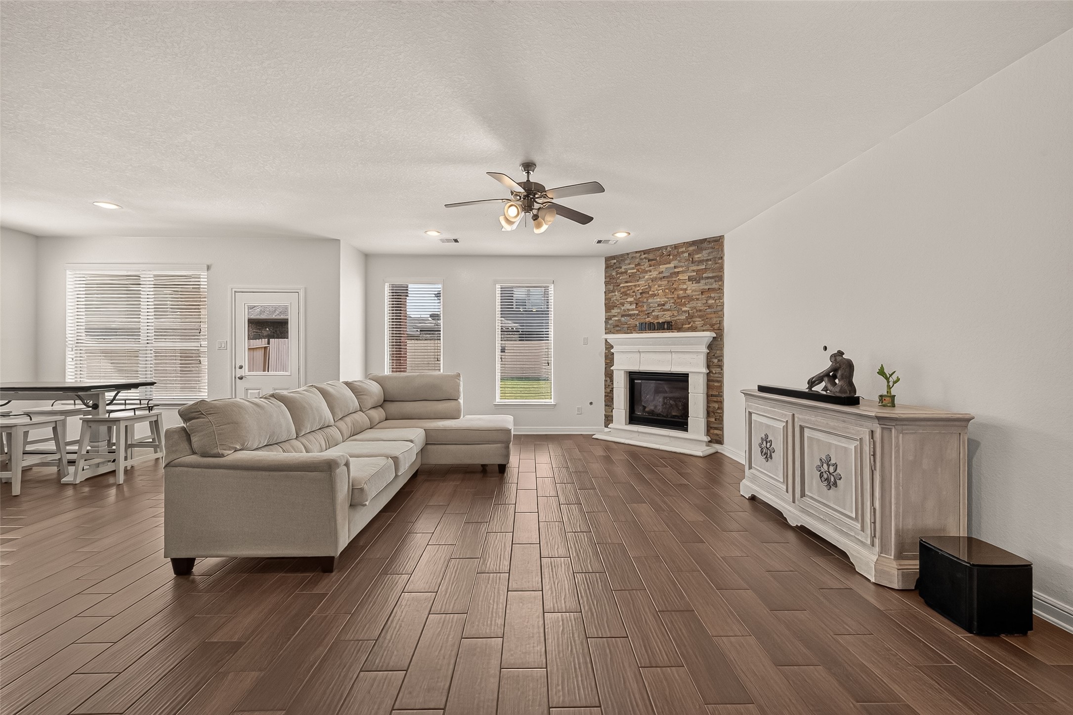 Spacious living area featuring a cozy stone fireplace, elegant wood-look flooring, and abundant natural light from large windows.