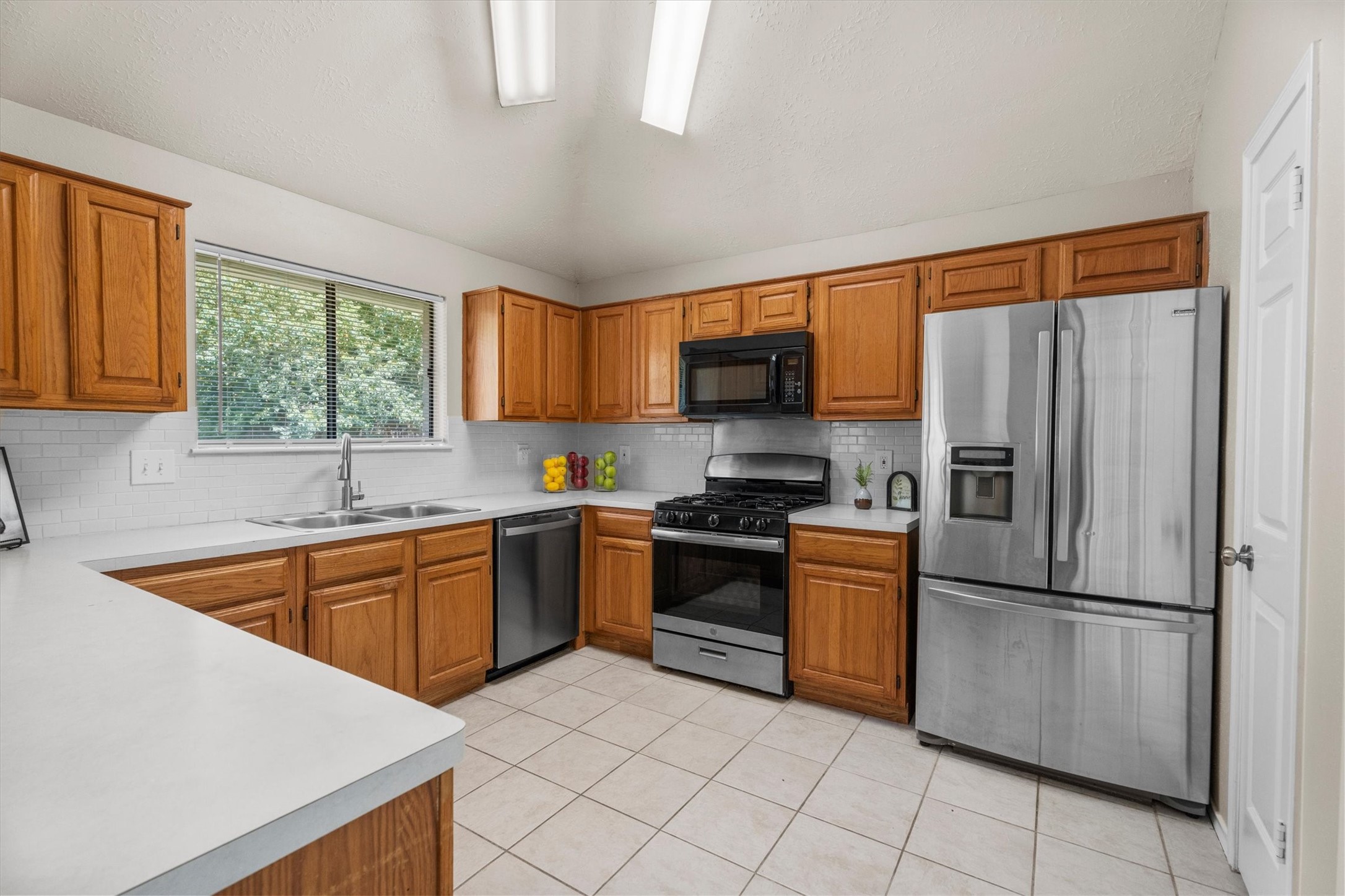 The kitchen features generous cabinetry, bright countertops, subway tile backsplash, and stainless-steel appliances.