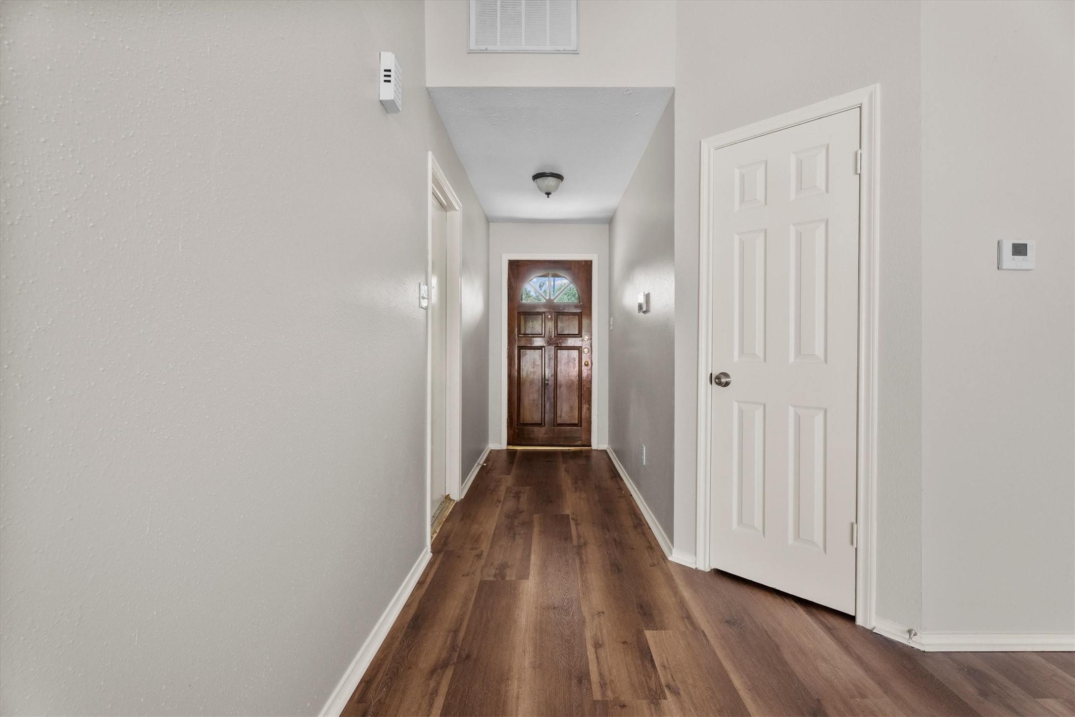 The bright entry hallway features wood-look flooring, neutral finishes, and a decorative front door.