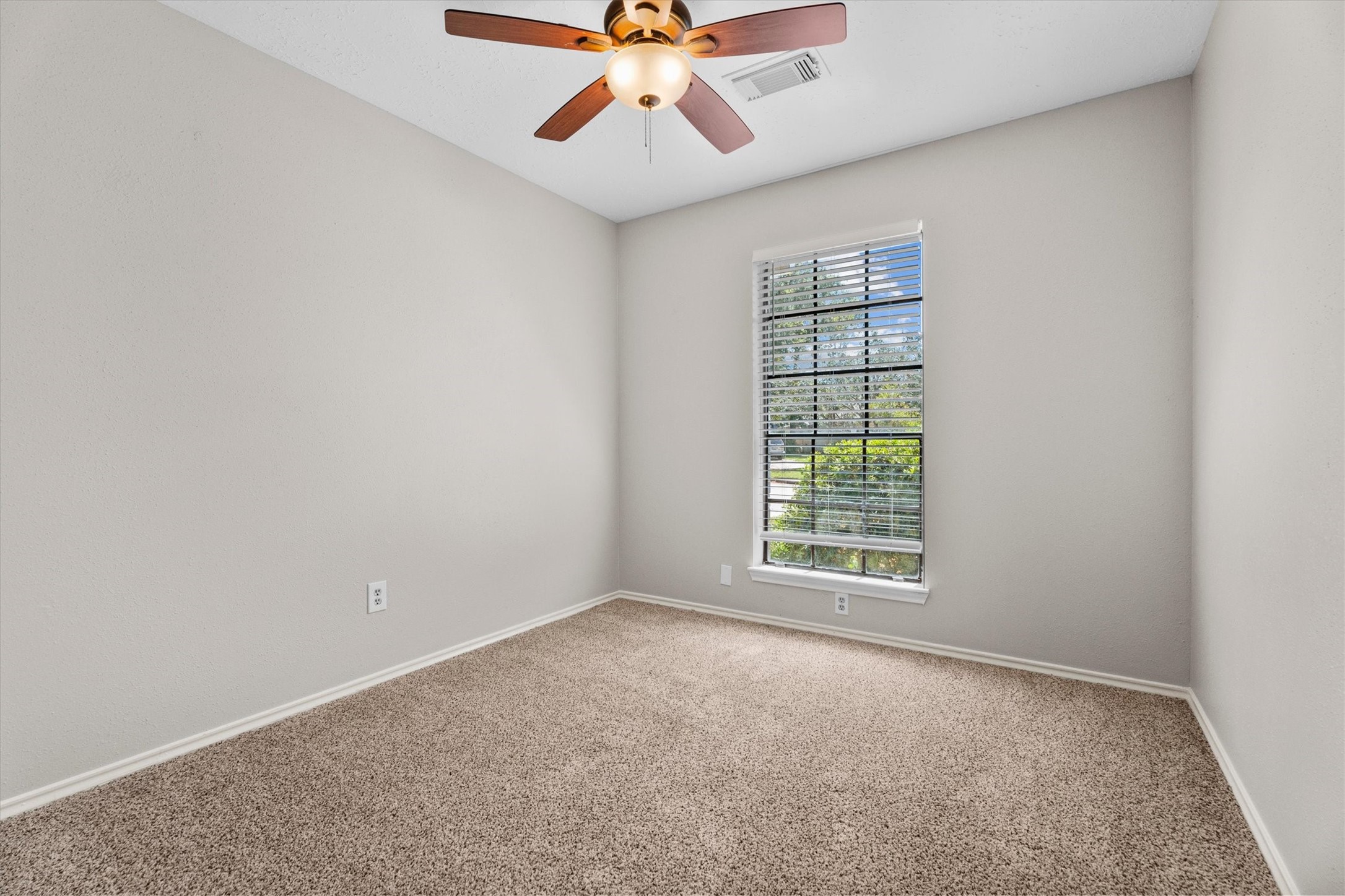 Secondary bedroom featuring a ceiling fan, plush carpeting, and a large window with natural light.