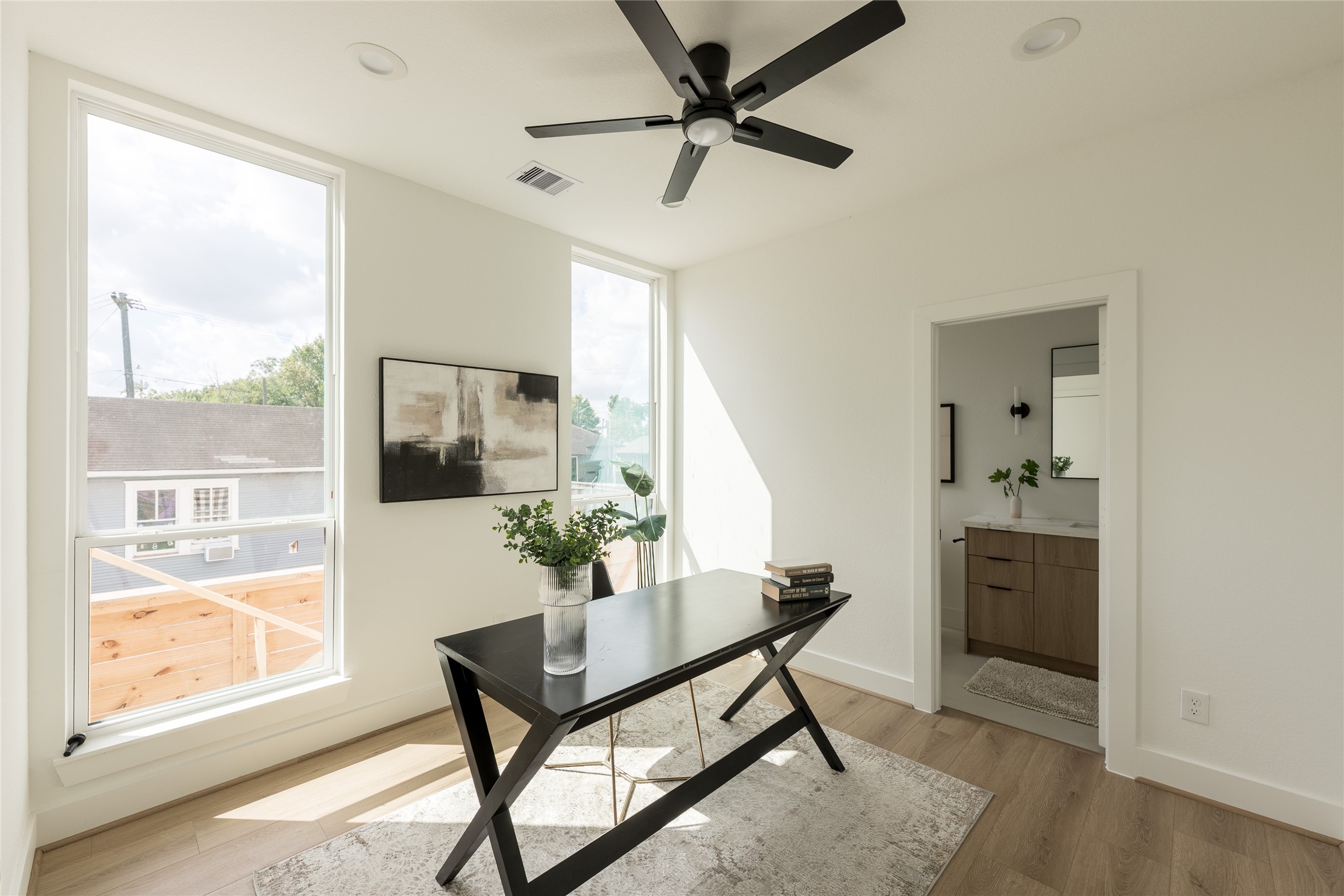 Bright, modern office space with large windows, sleek ceiling fan, and direct access to a stylish bathroom. Bright, modern office space with large windows, sleek ceiling fan, and direct access to a stylish bathroom.