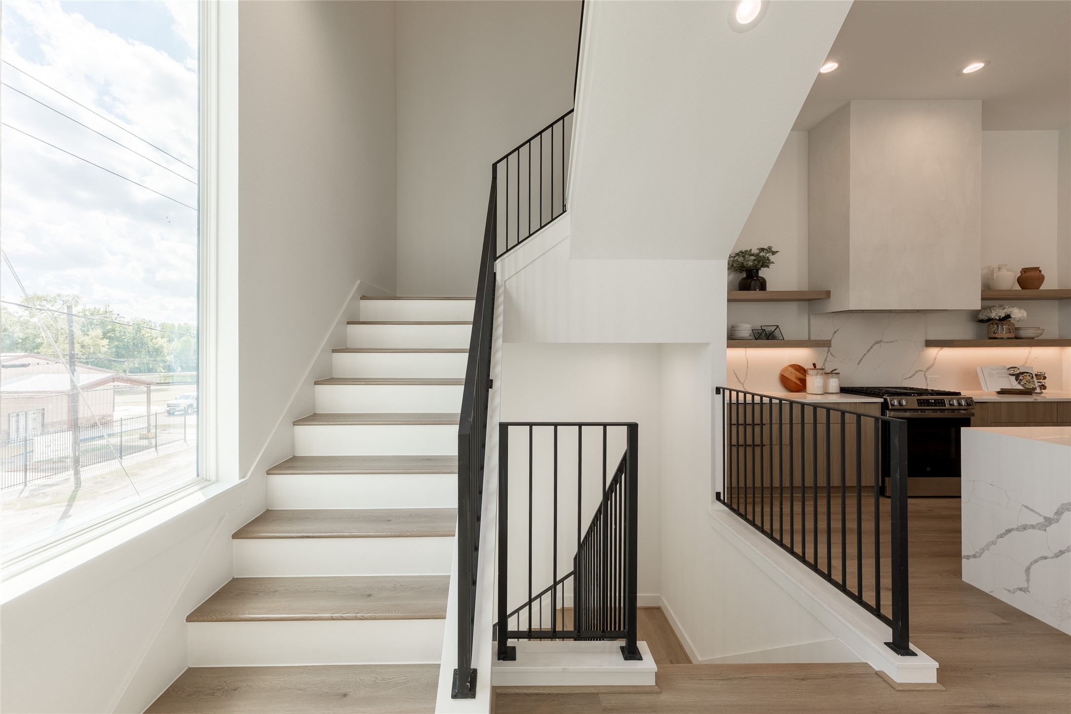 Bright and modern staircase with sleek black railings, adjacent to a stylish kitchen featuring open shelving and contemporary finishes.