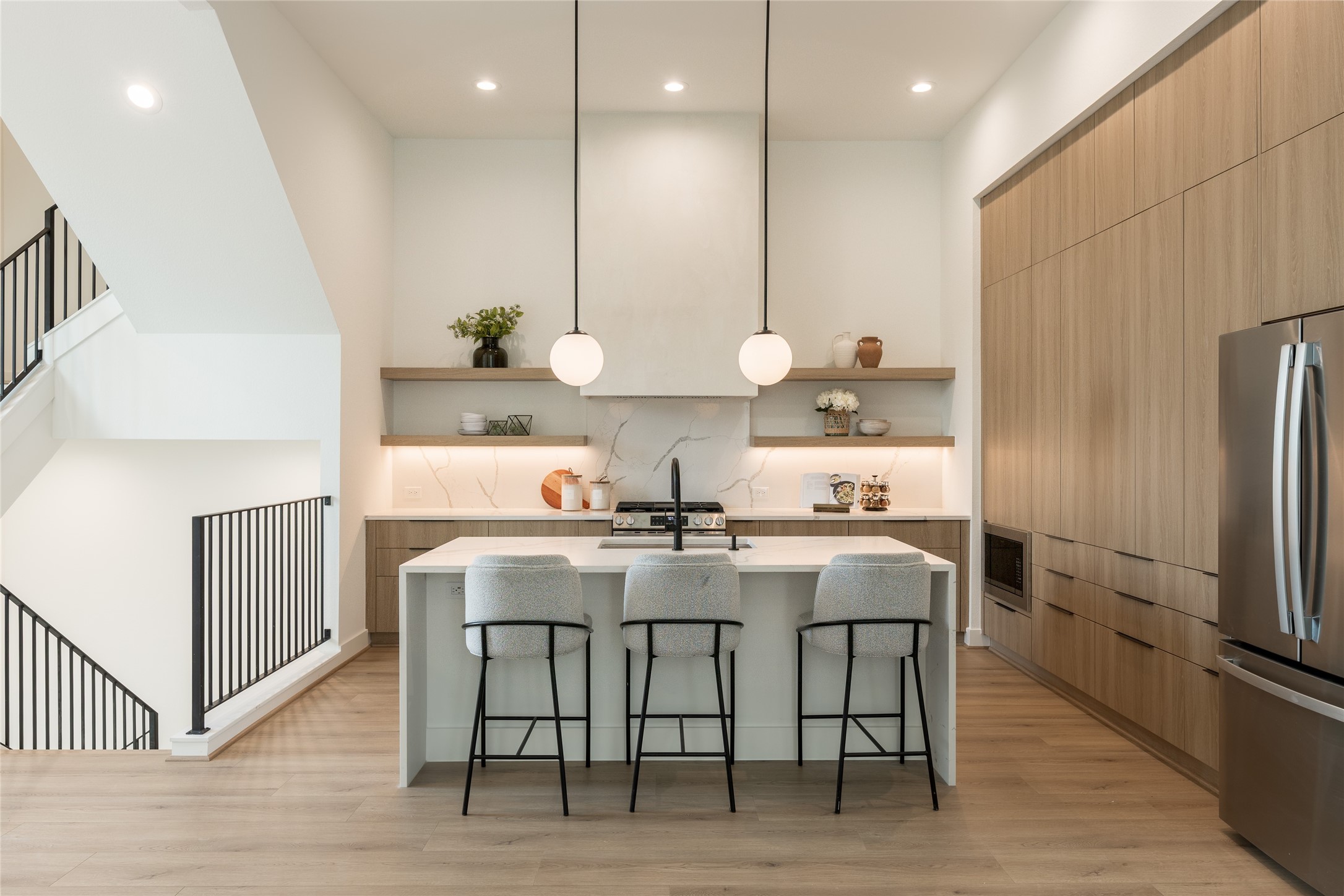 Modern kitchen with sleek wood cabinetry, a spacious waterfall island with seating, and stylish pendant lighting.