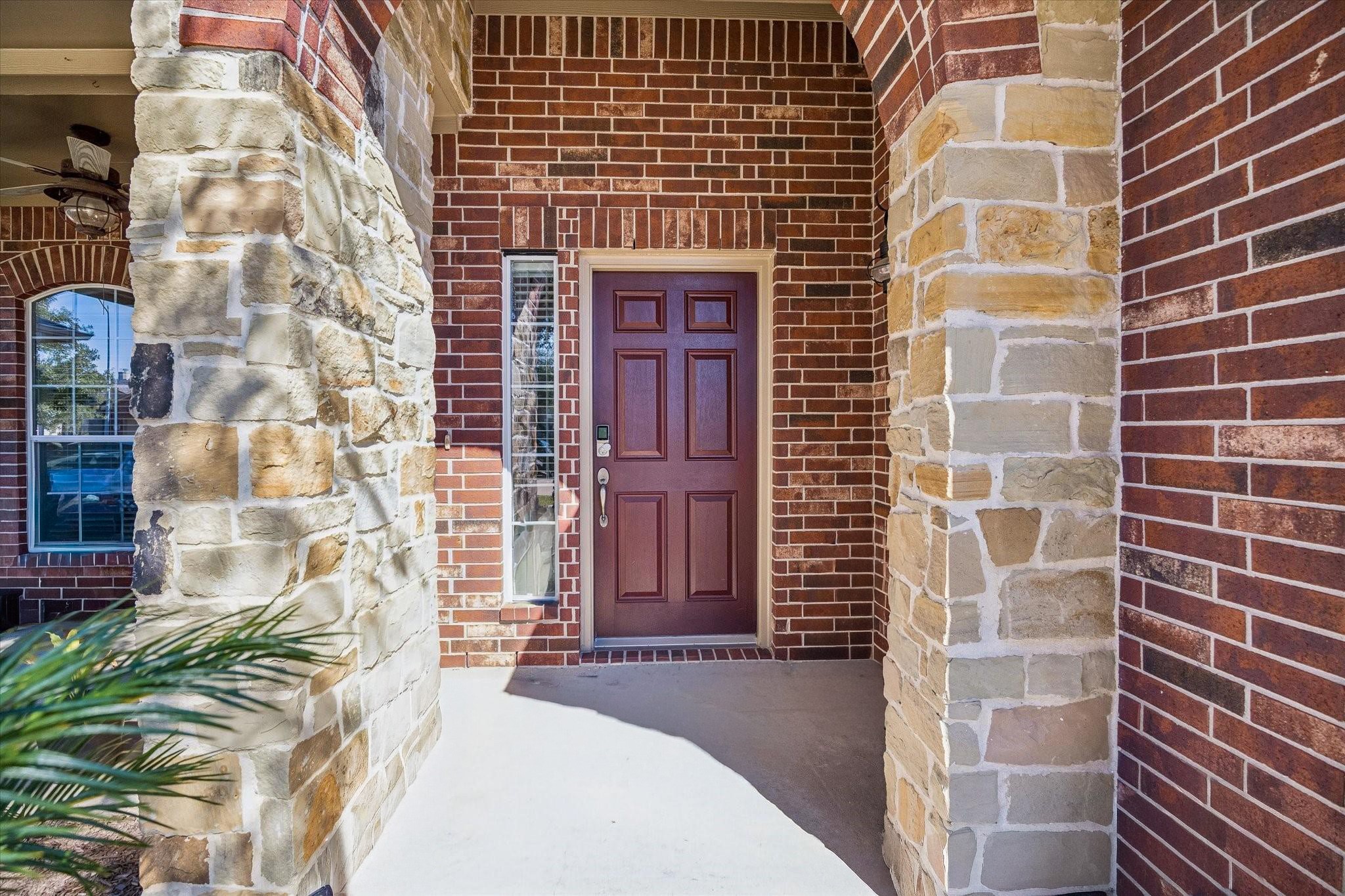 A covered front porch and beautiful wood-tone door create a warm welcome for guests. The arched entry and natural stone accents add character before you even step inside.