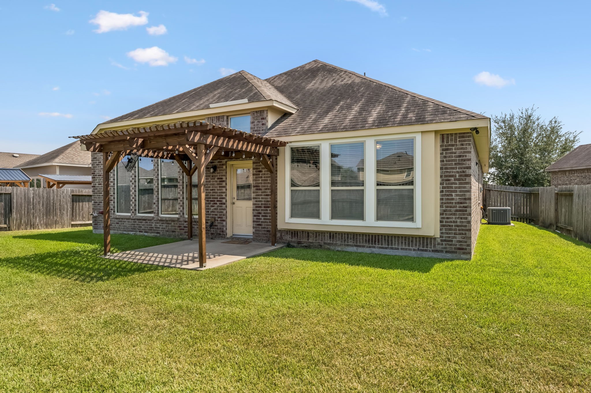 Charming brick home with a spacious backyard, featuring a lovely pergola-covered patio perfect for outdoor relaxation.