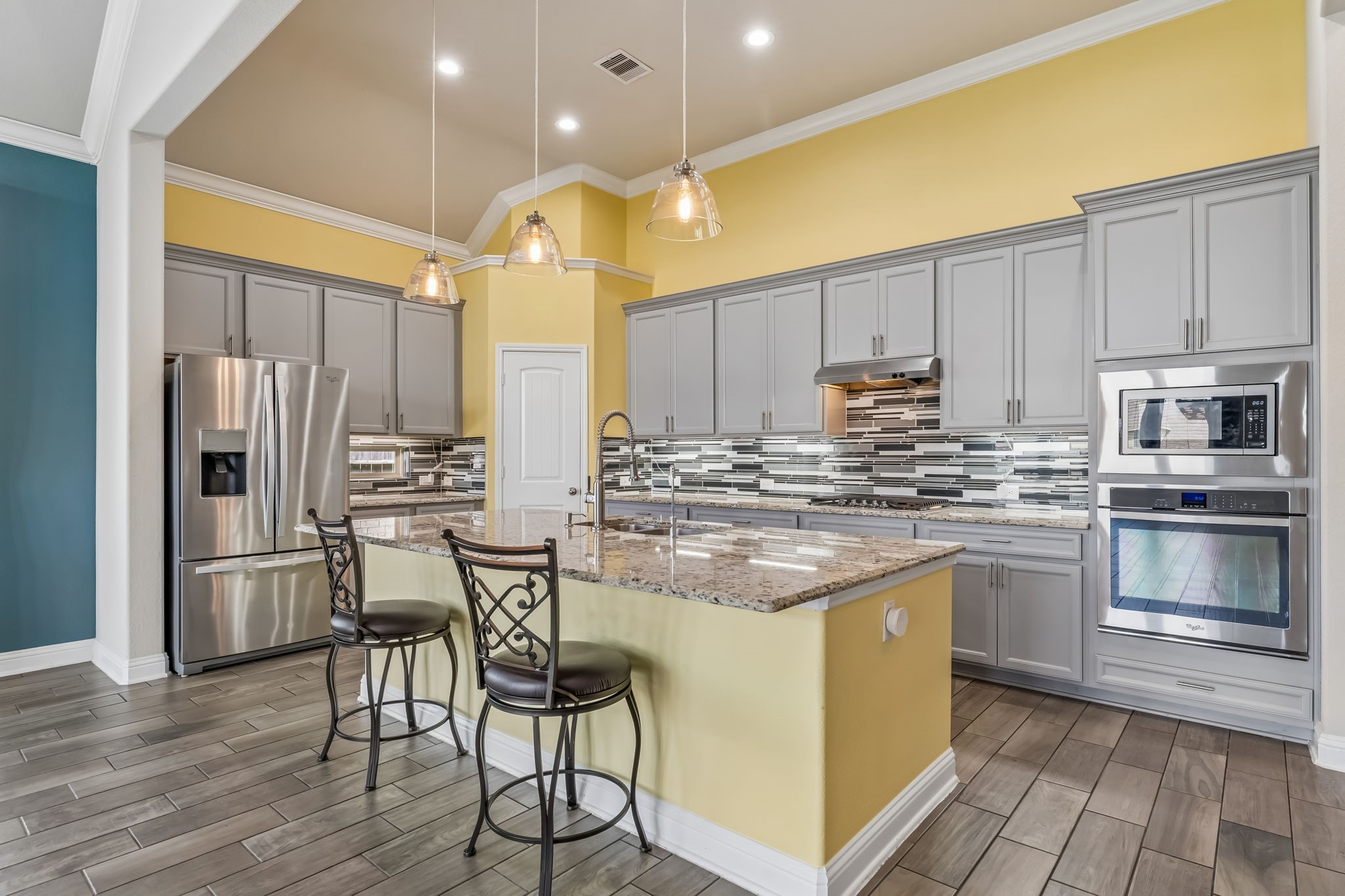 Bright and modern kitchen with sleek gray cabinetry, stainless steel appliances, and a stylish mosaic backsplash. The spacious island provides ample workspace and seating, perfect for entertaining.