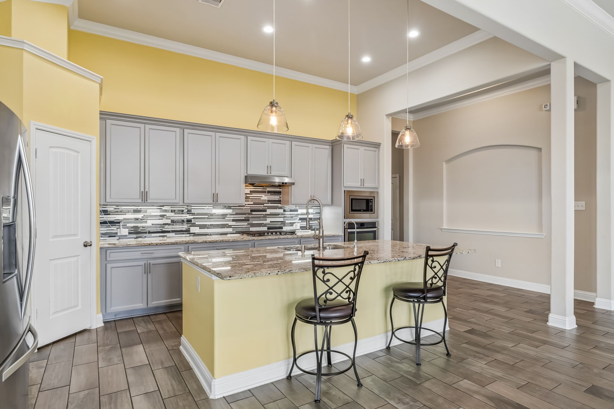 Bright and spacious kitchen featuring sleek gray cabinetry, a stylish tile backsplash, and a large granite island with seating.