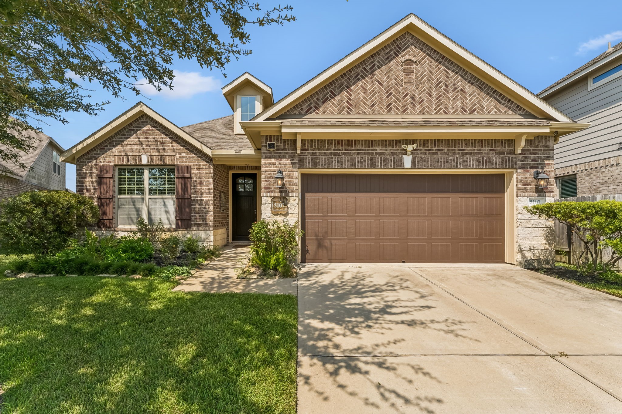 Charming brick home with a welcoming front porch, neatly manicured lawn, and a spacious two-car garage.