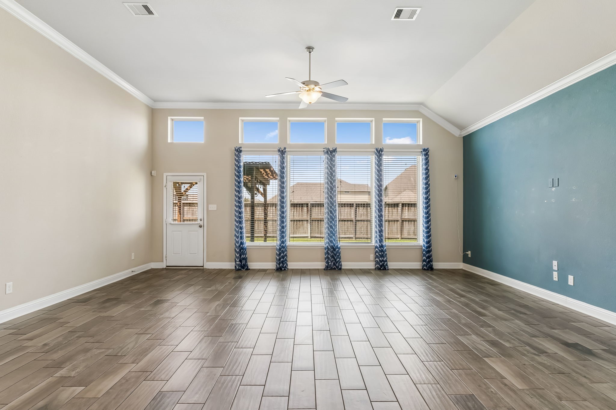 Spacious living area with high ceilings, large windows for natural light, and elegant wood-look tile flooring.