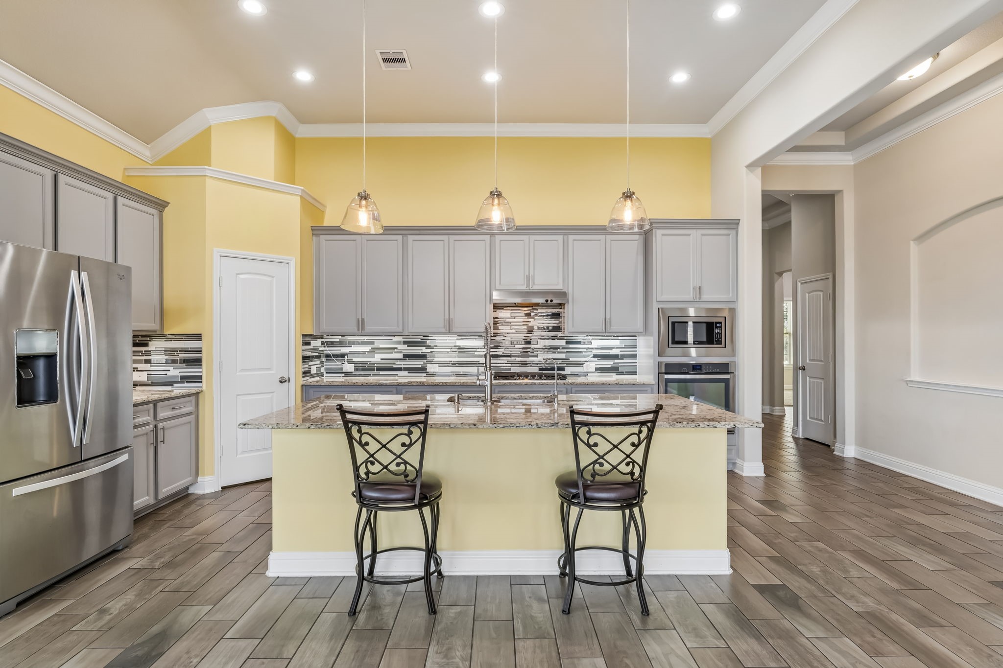Elegant kitchen with modern stainless steel appliances, a spacious island with seating, and stylish pendant lighting. The sleek backsplash and warm color palette create a welcoming atmosphere.