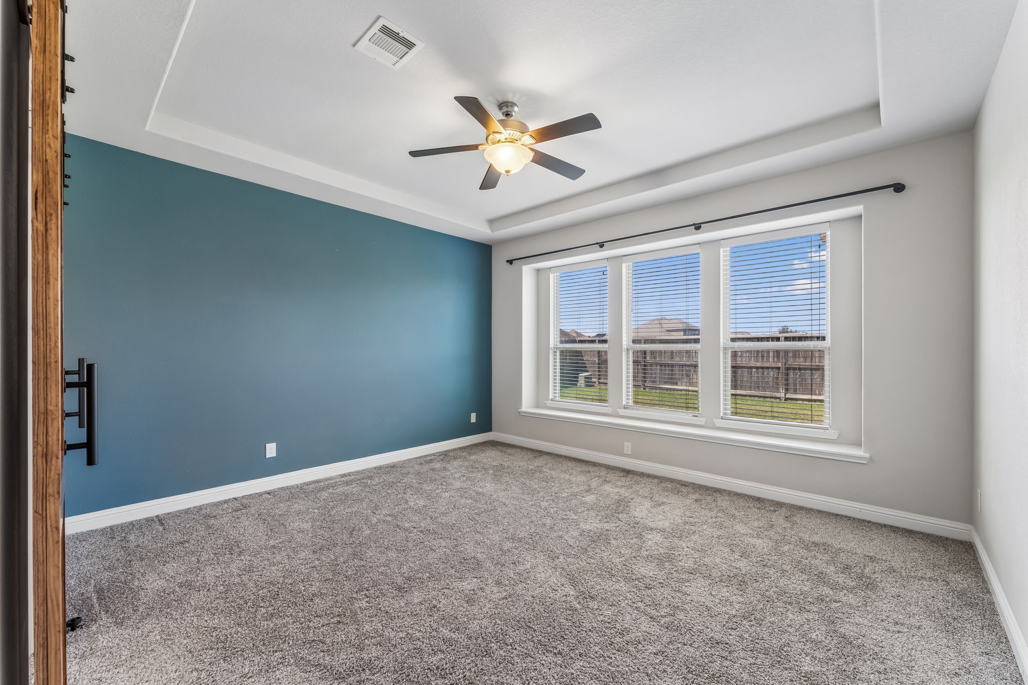 Spacious primary bedroom featuring a soothing blue accent wall, plush carpeting, and large windows that provide abundant natural light.