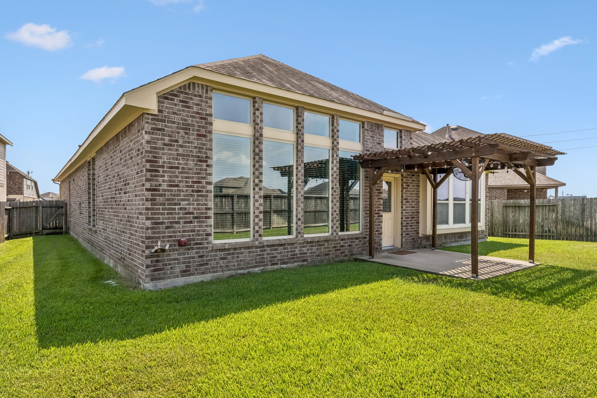 Charming brick home with large windows and a cozy pergola-covered patio, set in a spacious, well-maintained backyard.