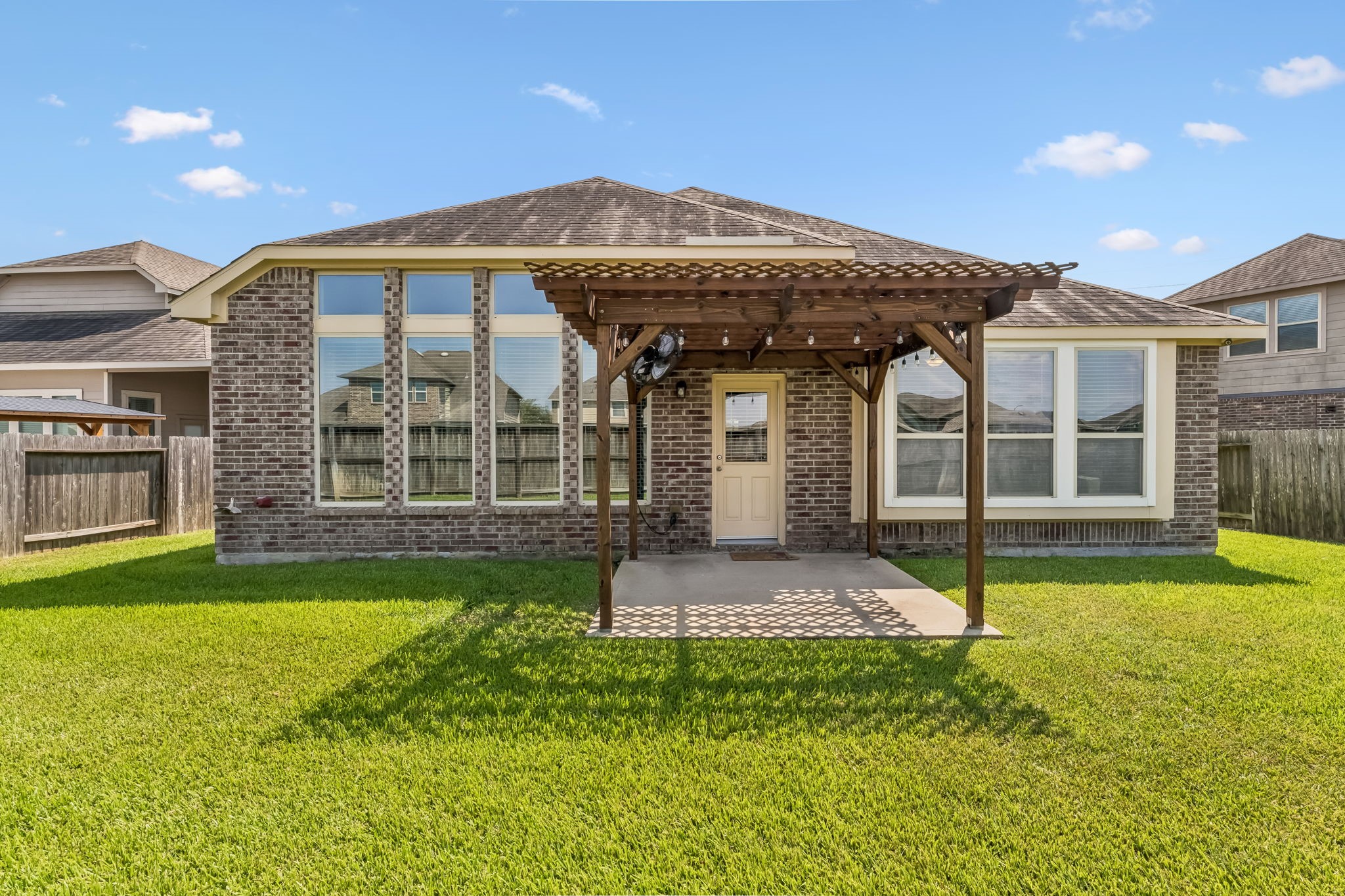 Charming brick exterior with large windows and a cozy pergola-covered patio, perfect for outdoor relaxation in the spacious backyard.