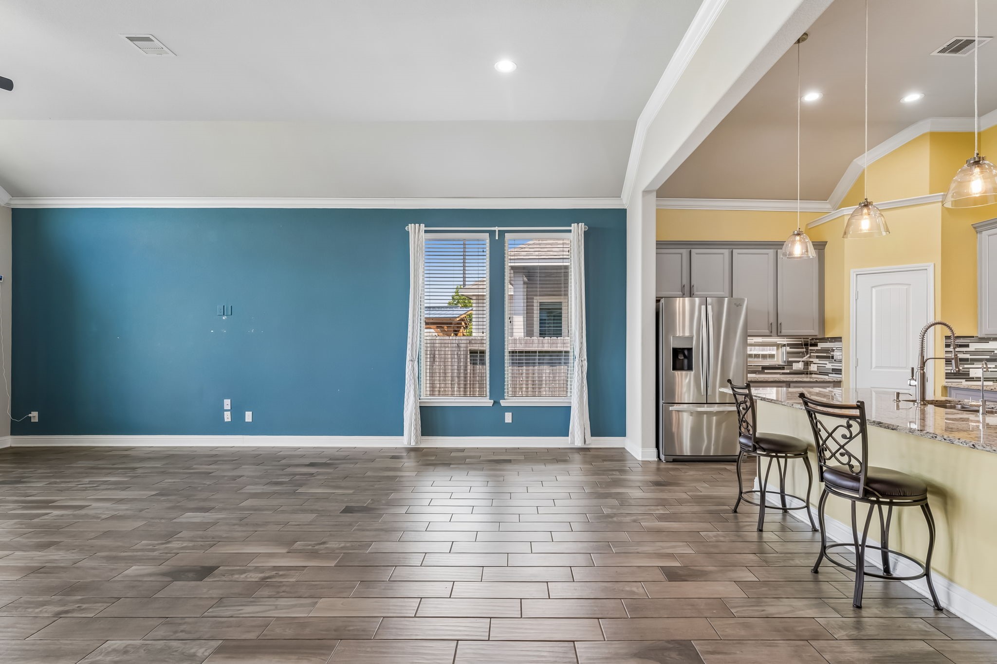 Spacious open-concept living area with elegant tile flooring, vibrant accent wall, and a modern kitchen featuring stainless steel appliances and a large breakfast bar.