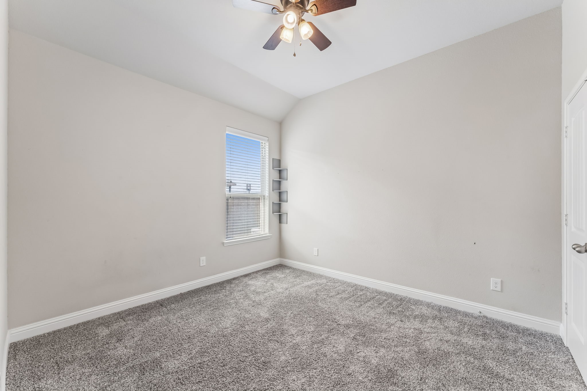 A cozy bedroom with soft carpeting, neutral walls, a ceiling fan, and ample natural light from the window, perfect for relaxation.