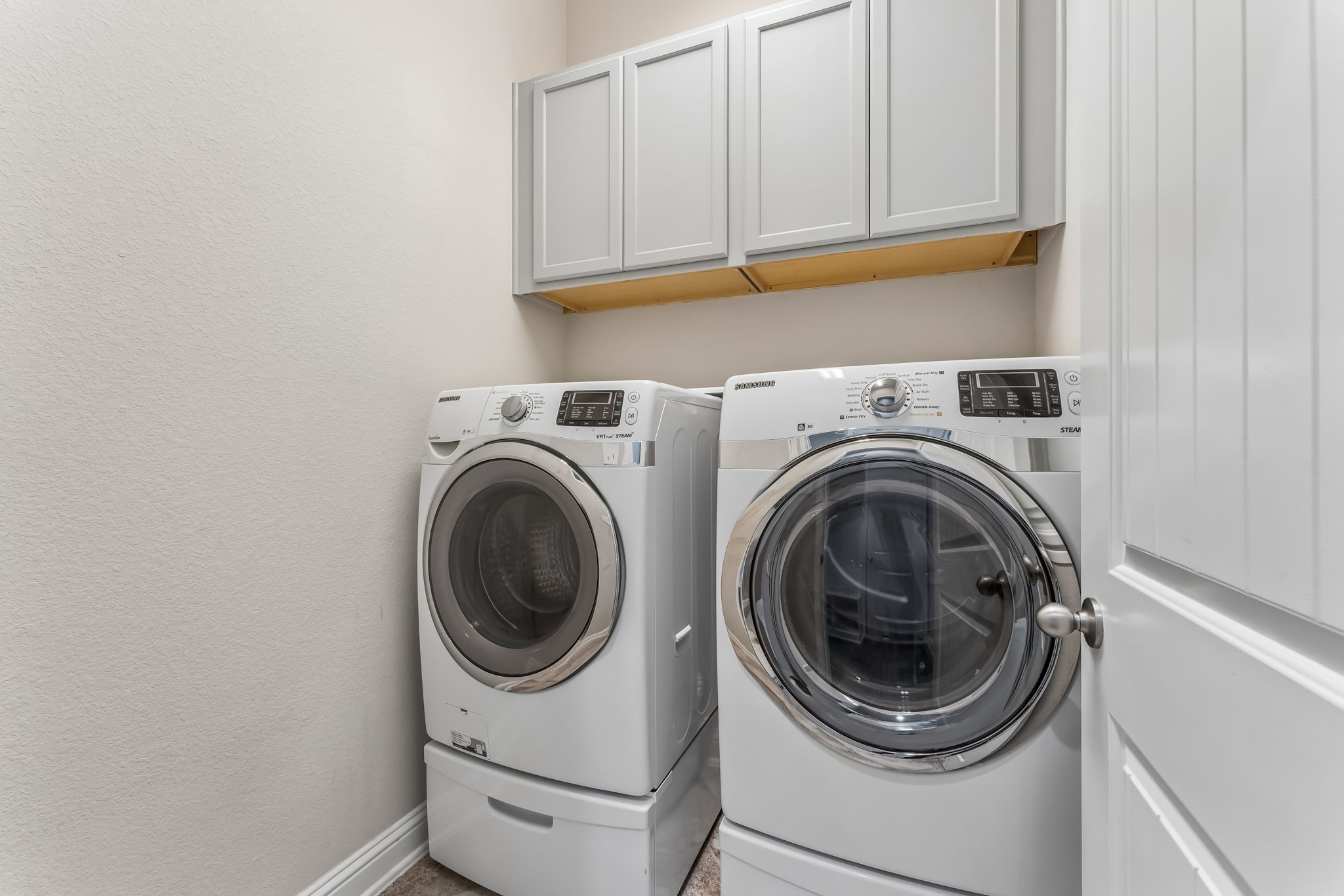 Modern laundry room featuring a high-efficiency washer and dryer set, complemented by ample overhead storage cabinets.