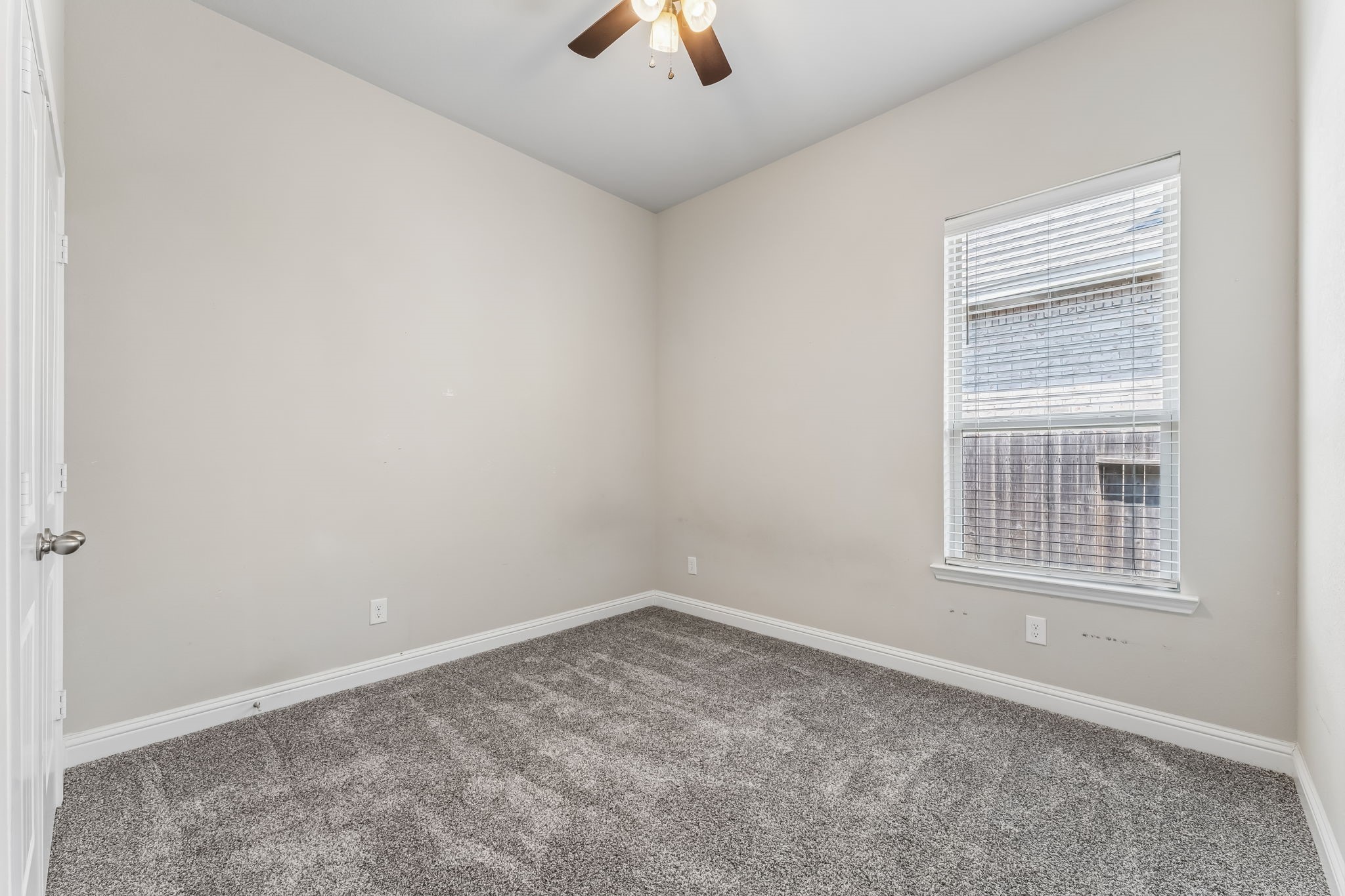 Cozy bedroom with soft carpeting, neutral walls, and a ceiling fan, filled with natural light from a large window.