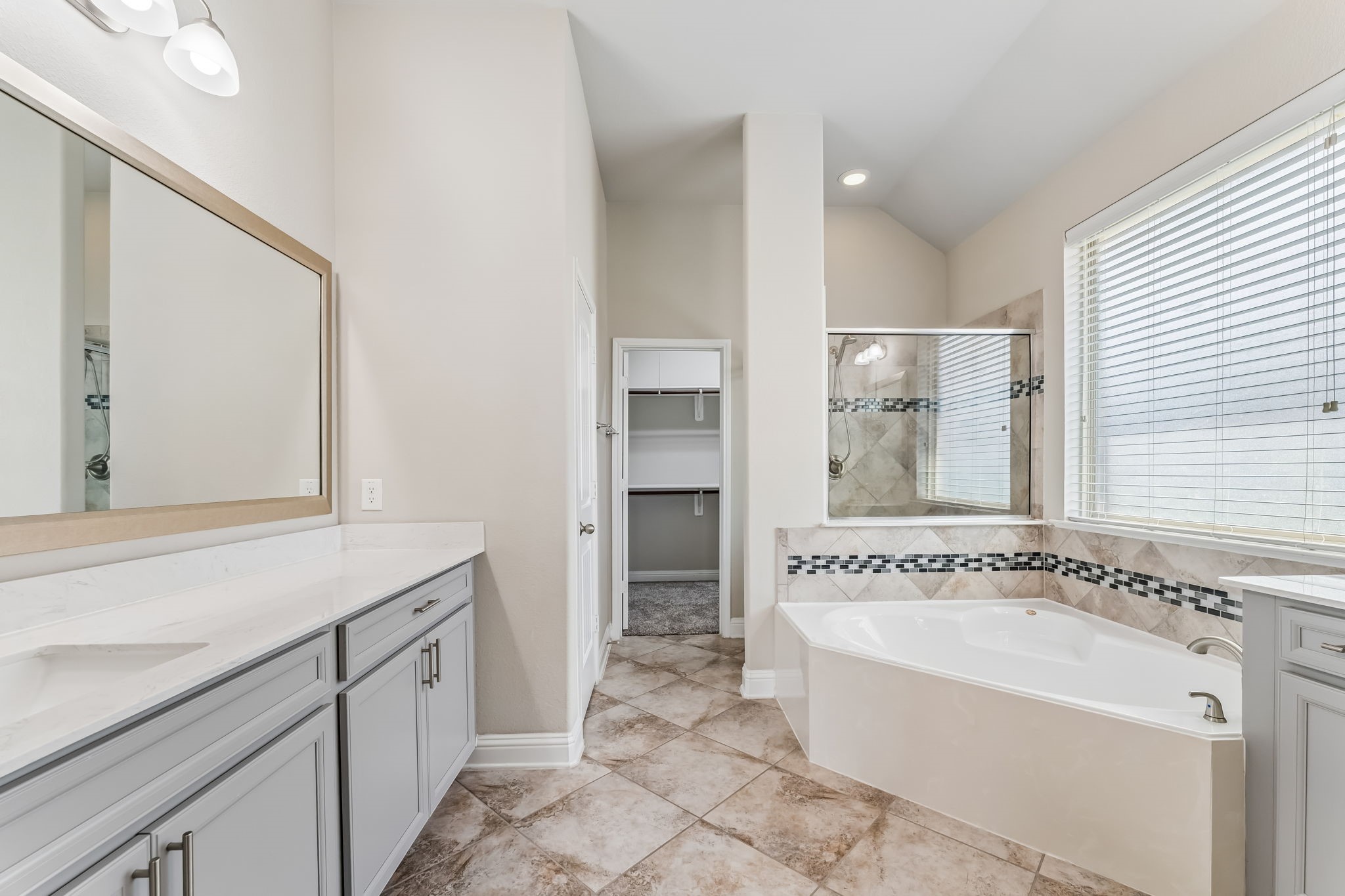 Elegant bathroom featuring a spacious soaking tub, dual sinks with stylish cabinetry, and a walk-in closet, all accentuated by natural light.