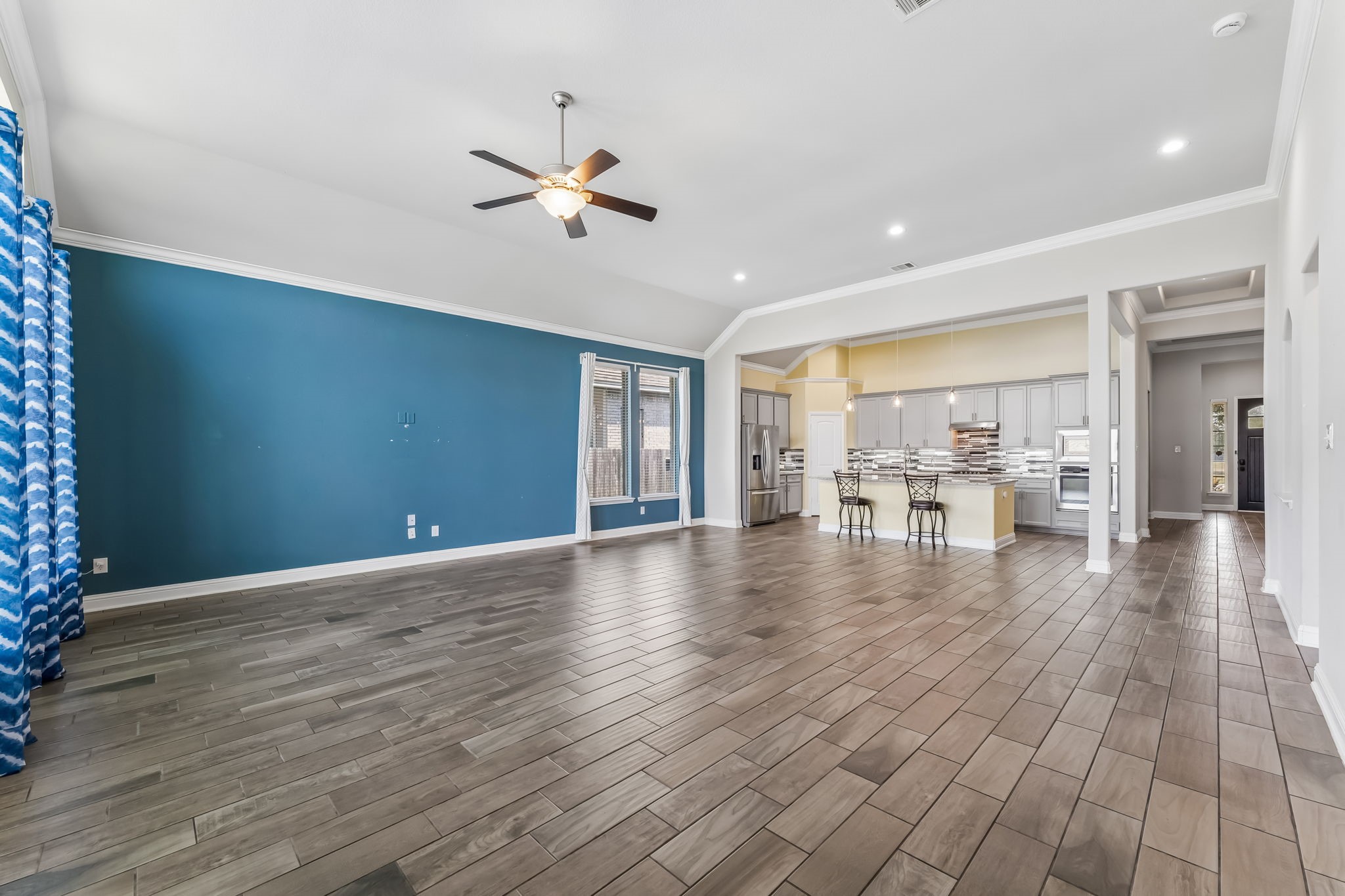 Spacious open-concept living area with sleek hardwood floors, a striking blue accent wall, and a modern kitchen featuring stainless steel appliances and a large island with bar seating.