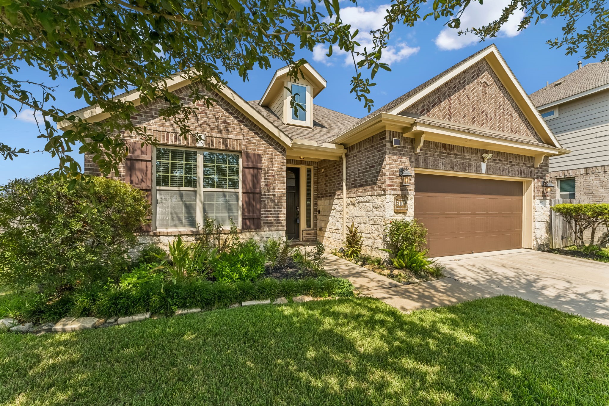 Charming brick home with a welcoming front porch and manicured landscaping, featuring a spacious two-car garage and a neatly maintained front yard.