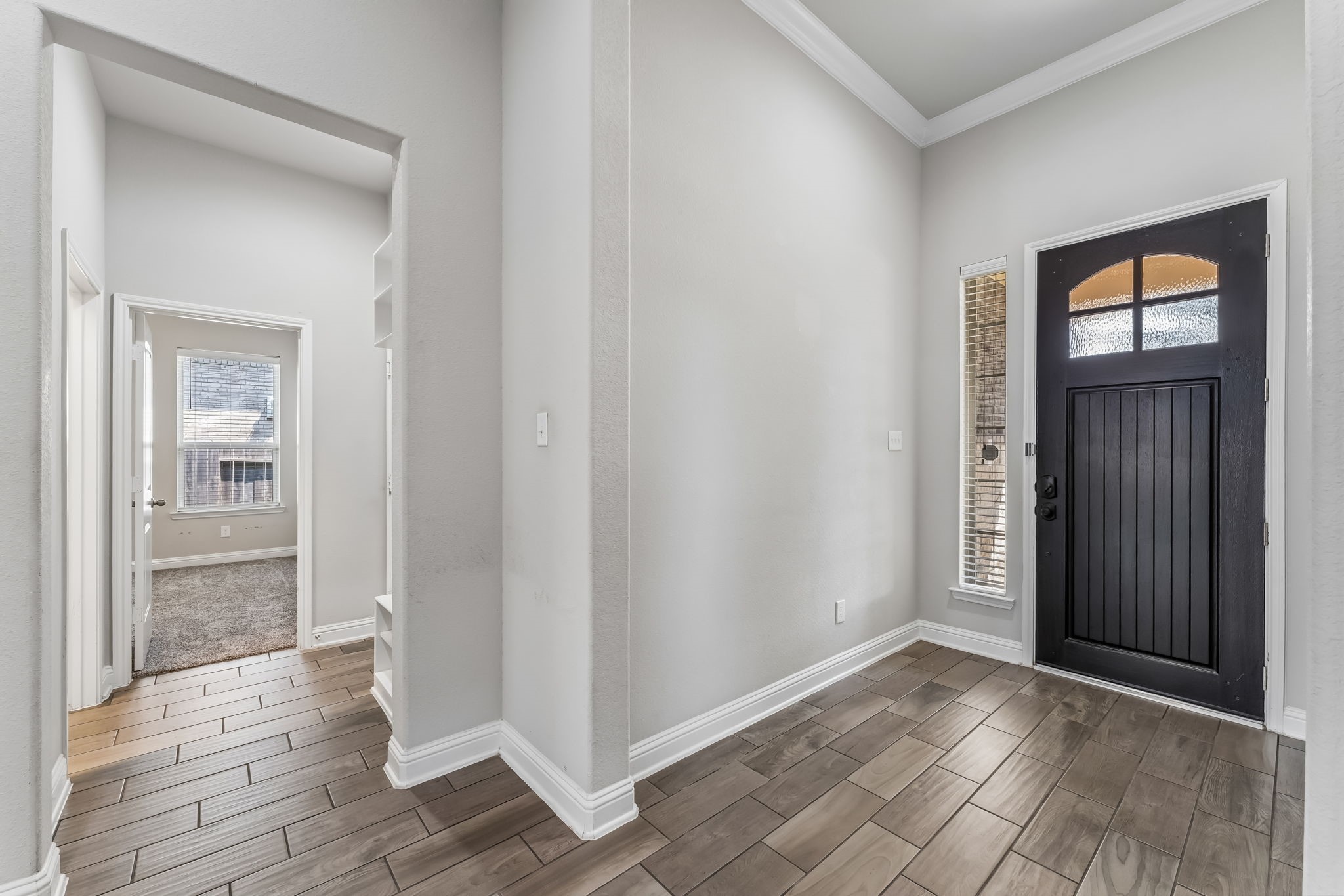 Inviting entryway featuring a dark wood front door, elegant tile flooring, and abundant natural light from tall windows, leading seamlessly to the rest of the home.