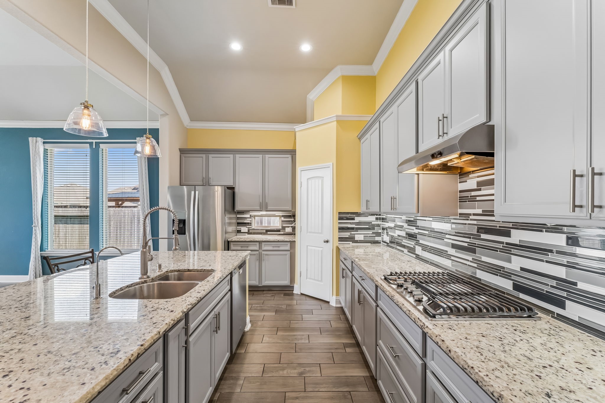 Spacious kitchen with granite countertops, modern stainless steel appliances, and elegant pendant lighting, complemented by stylish cabinetry and a chic tile backsplash.