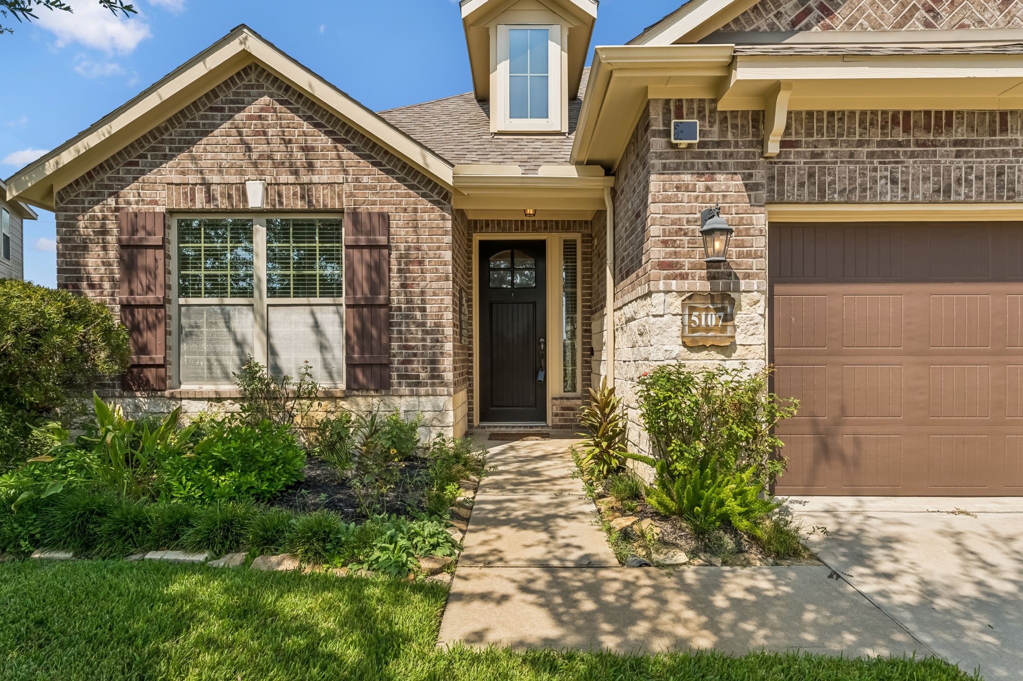 Charming brick exterior with a welcoming front porch, accented by lush landscaping and a classic lantern light.