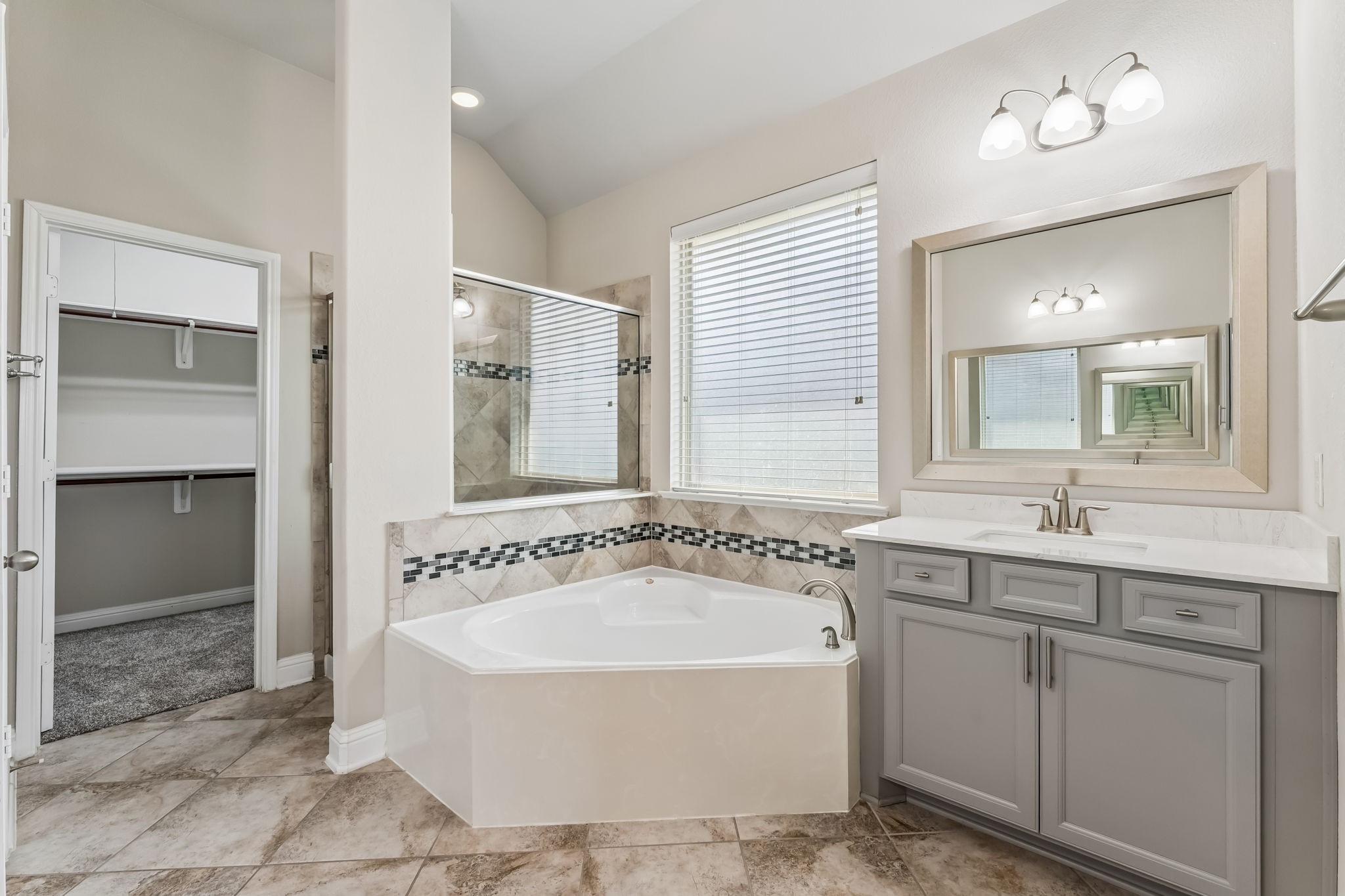 Elegant bathroom with a luxurious soaking tub, dual sinks, and stylish tile accents. Ample natural light enhances the spacious feel, and the walk-in closet offers convenient storage.