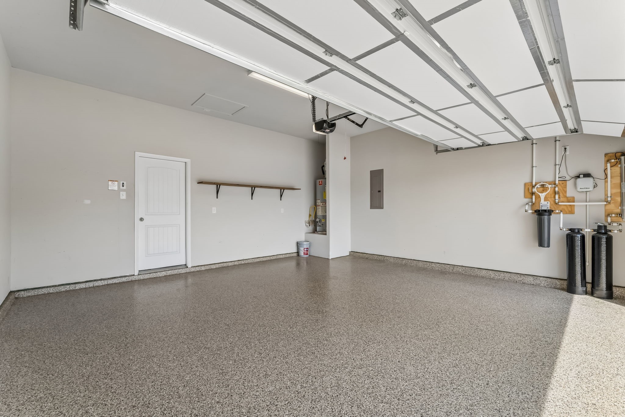 Spacious garage with a sleek epoxy floor, built-in storage shelf, modern utility systems, and epoxy flooring, perfect for organization and functionality.