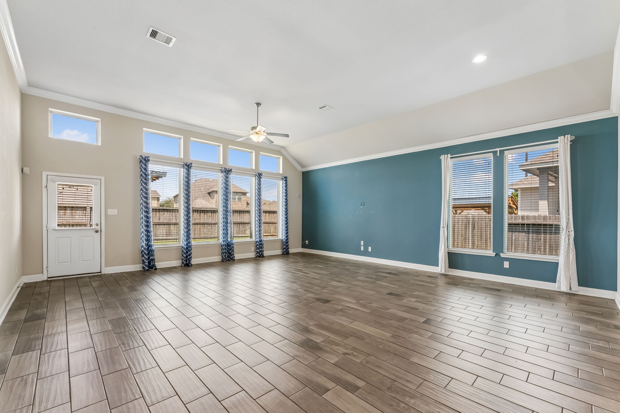 Spacious living area with high ceilings, large windows for natural light, and stylish wood-look tile flooring, perfect for entertaining and relaxation.