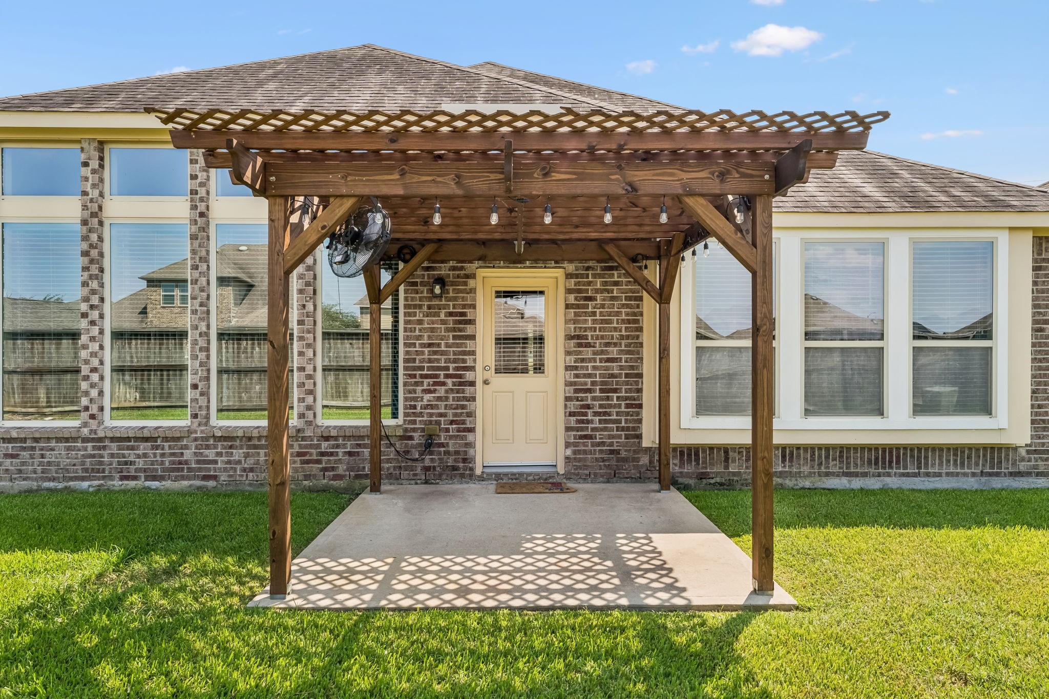 Charming backyard features a cozy pergola-covered patio, perfect for outdoor relaxation and entertaining, set against a backdrop of large windows that invite natural light into the home.