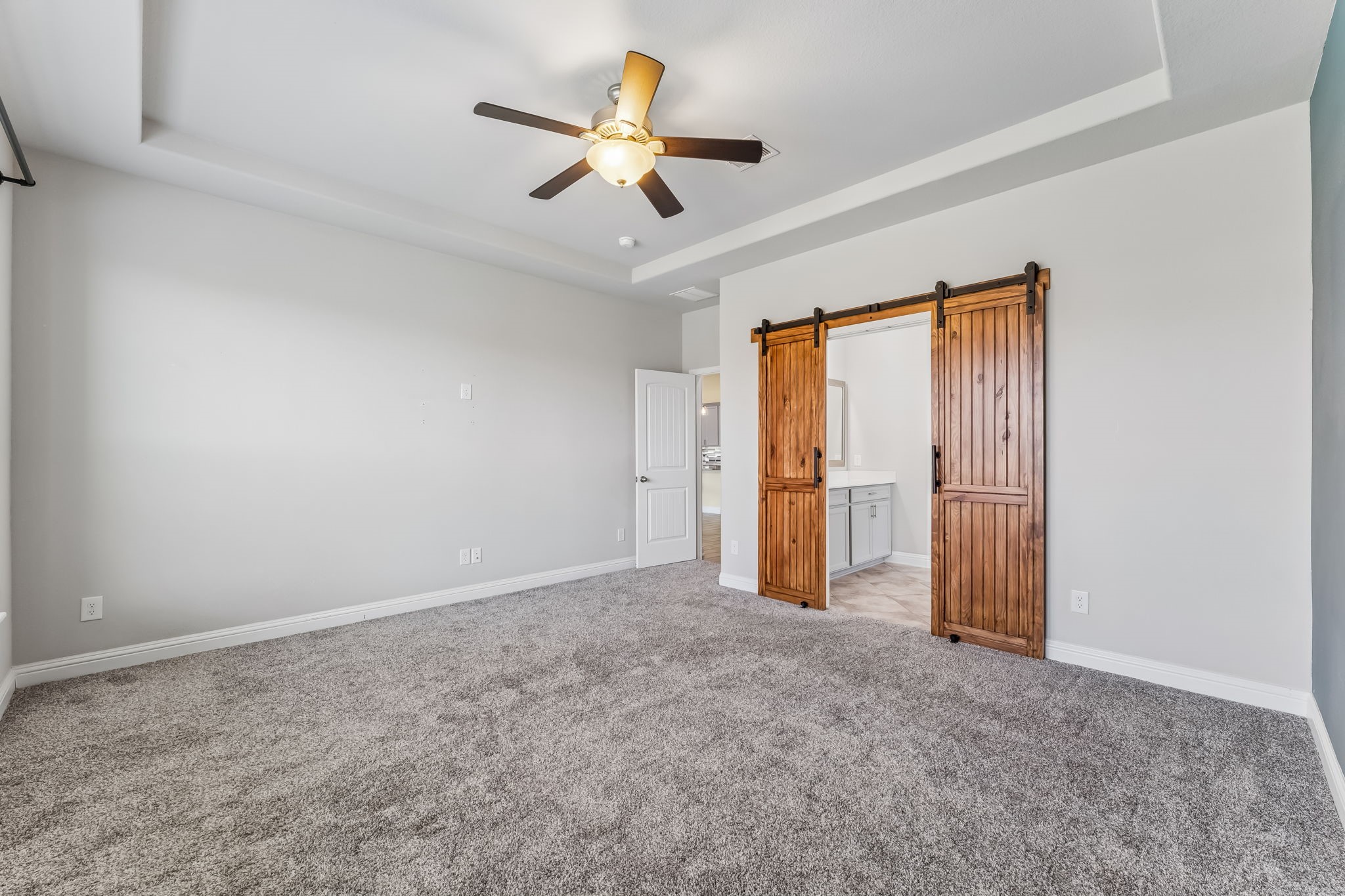 Spacious bedroom with plush carpeting, featuring a ceiling fan and charming wooden barn doors leading to an en-suite bathroom.