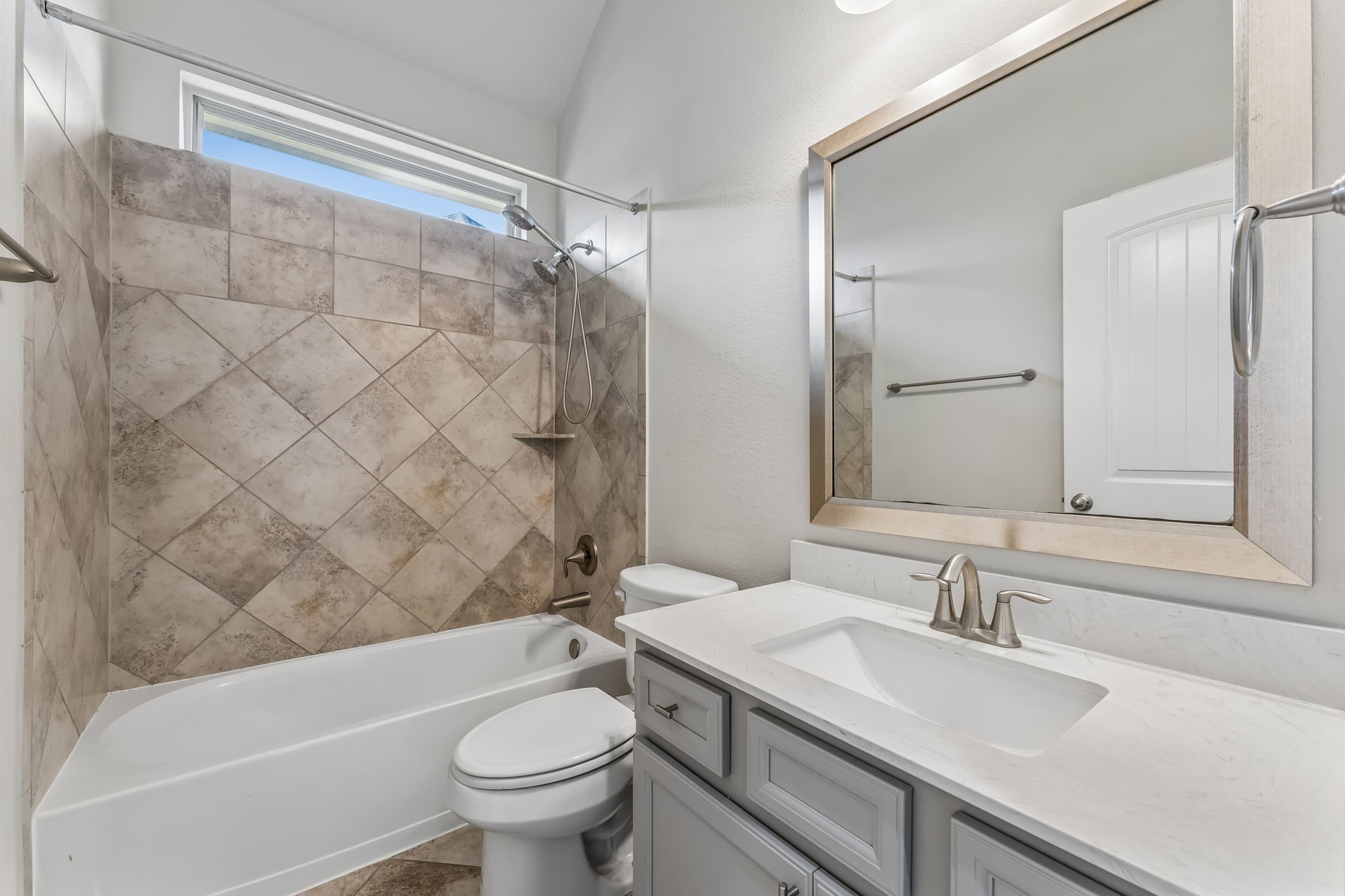 Charming bathroom featuring a tiled shower-bath combo, a sleek vanity with a modern faucet, and a large framed mirror.