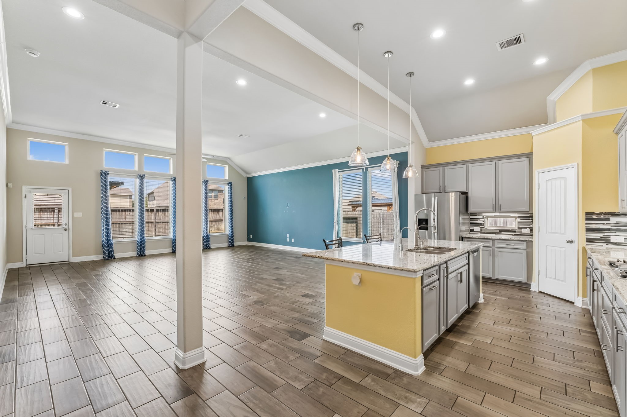 Open-concept living area with high ceilings, abundant natural light, and a modern kitchen featuring an island and stainless steel appliances.