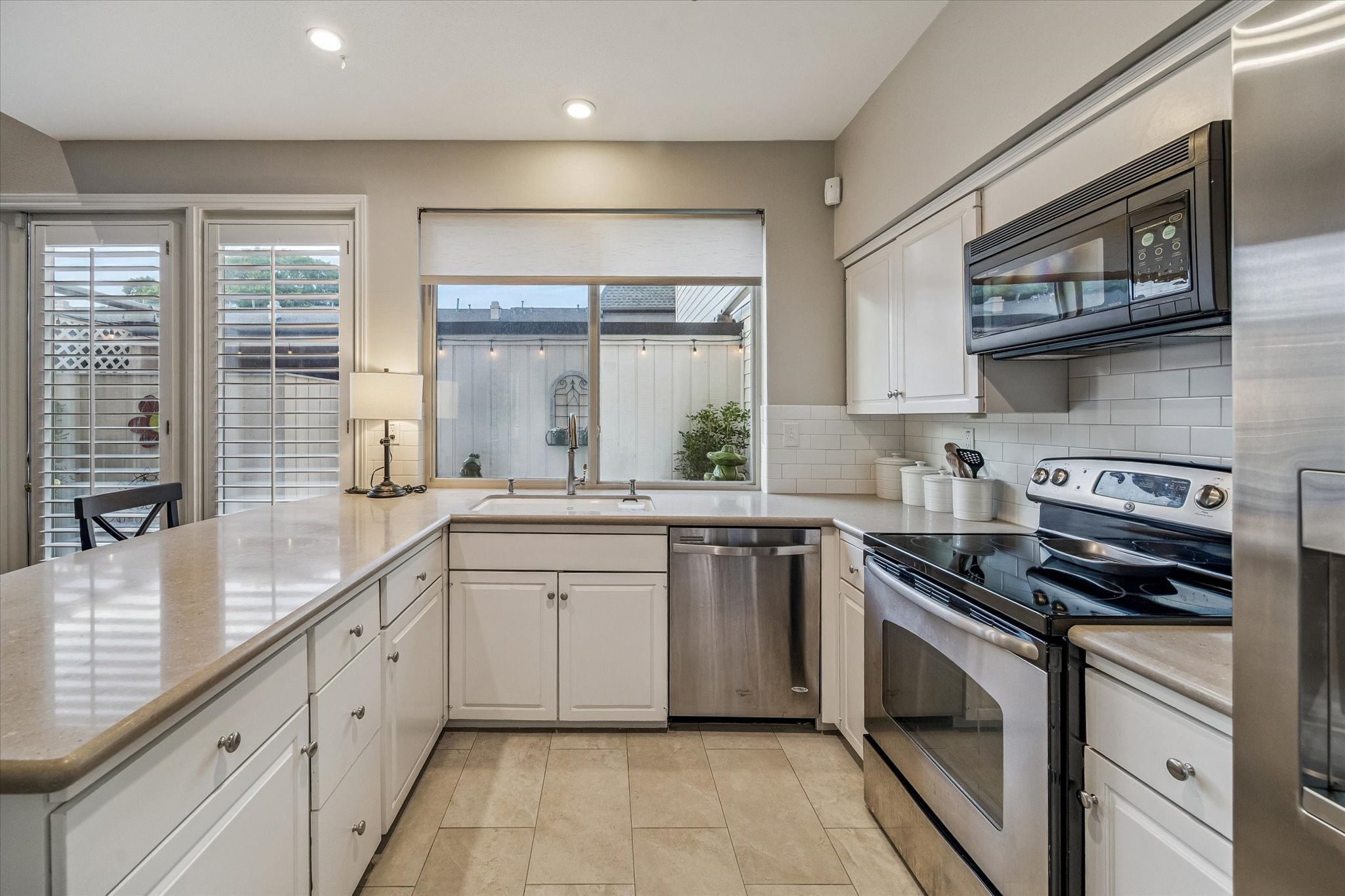 The remodeled Kitchen boasts Cesar Stone counters, subway tile backsplash, large under mount single basin porcelain sink w/ brushed faucet and cabinet hardware, stainless appliances including the refrigerator, travertine tile floors and coveted window views! Note the walk-in pantry and laundry room! NICE!