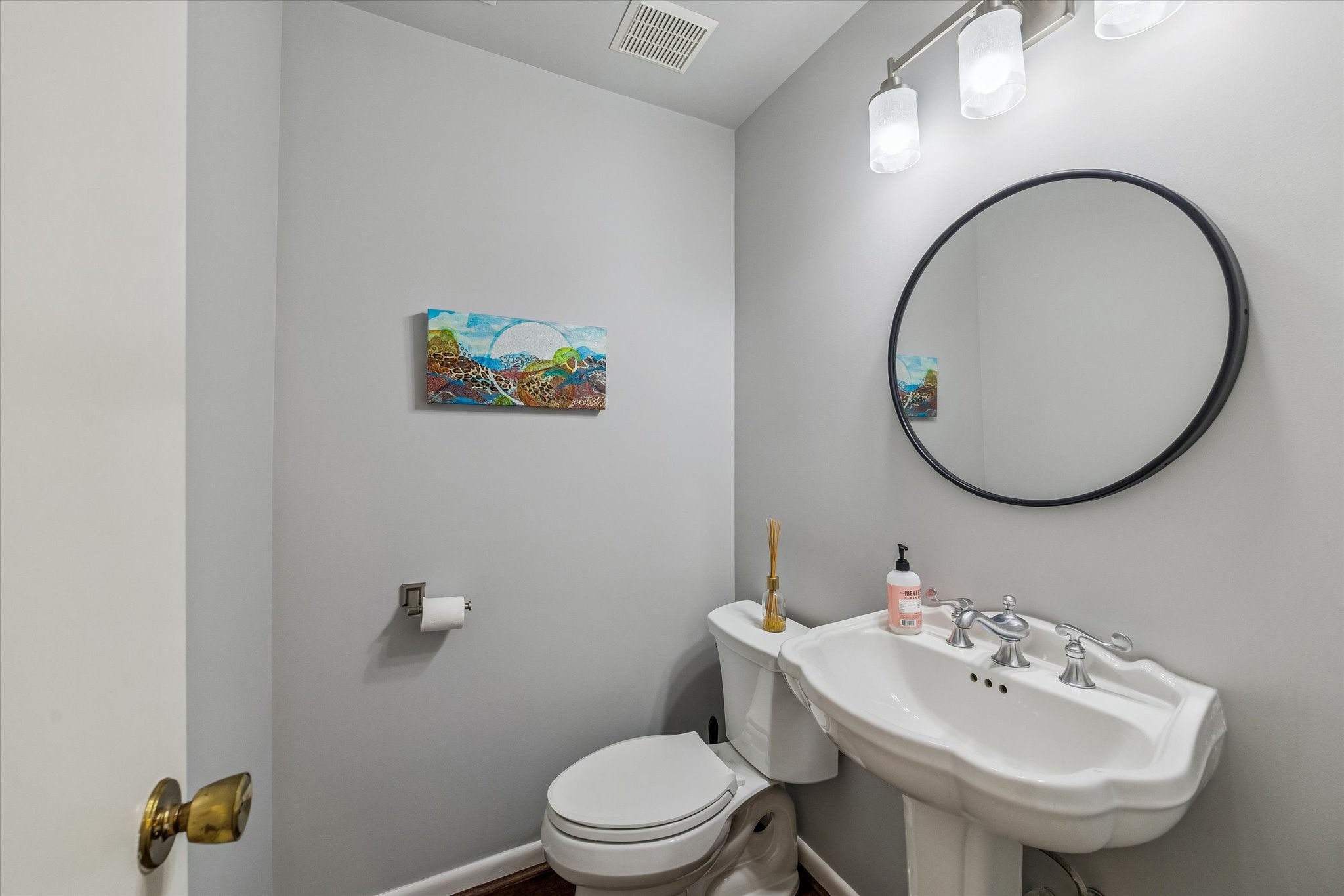 Cleverly located downstairs off the hall of Living/Dining Room, the remodeled Powder Room features a white porcelain  scalloped pedestal sink, decorative framed mirror, new light fixture, stylish wood floors and more!