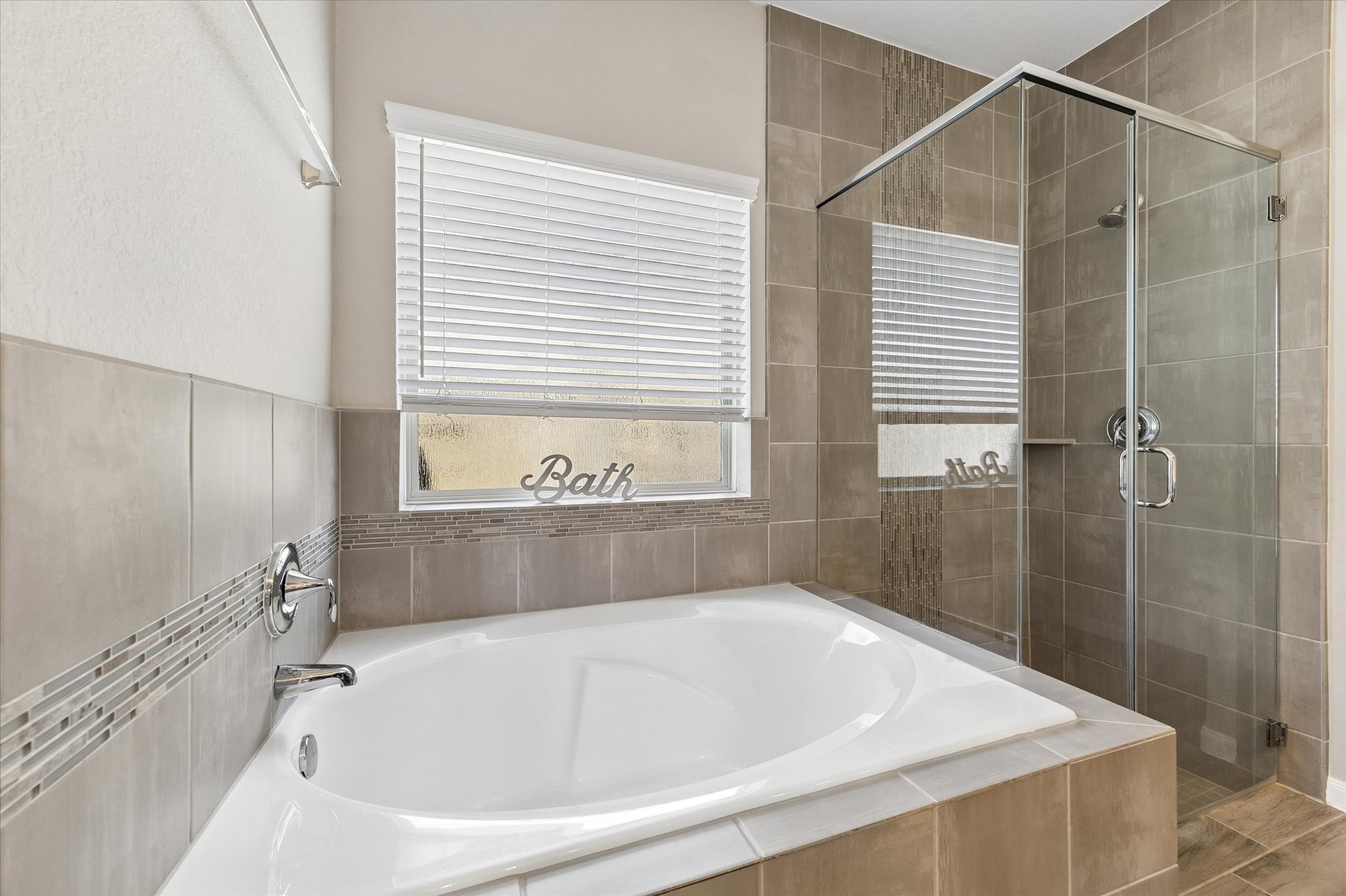 Enjoy a quiet reset in the soaking tub, positioned beside a separate glass-enclosed shower with coordinating tile surrounds.