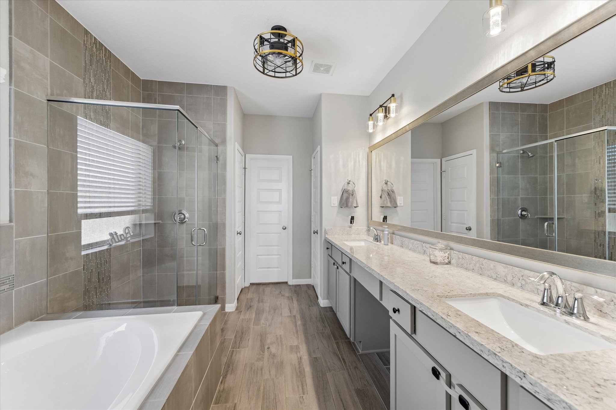The first-floor primary bathroom offers a spacious retreat with dual sinks, generous vanity storage, a soaking tub, and a separate glass-enclosed shower.