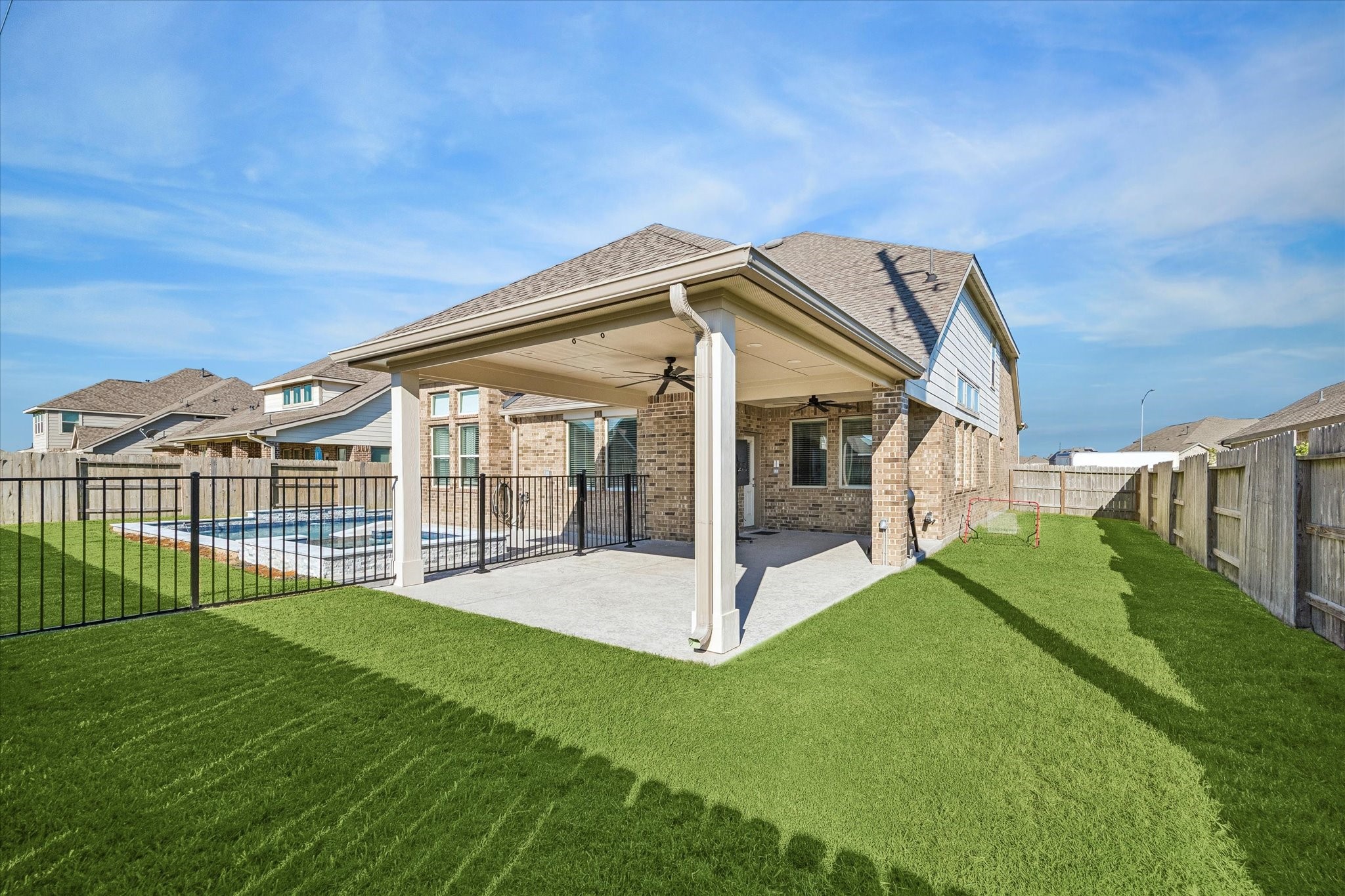 Room to swim, gather, and play. The extended covered patio overlooks a privacy-fenced backyard with lush Bermuda grass, replaced in 2024, and open lawn beyond the pool.