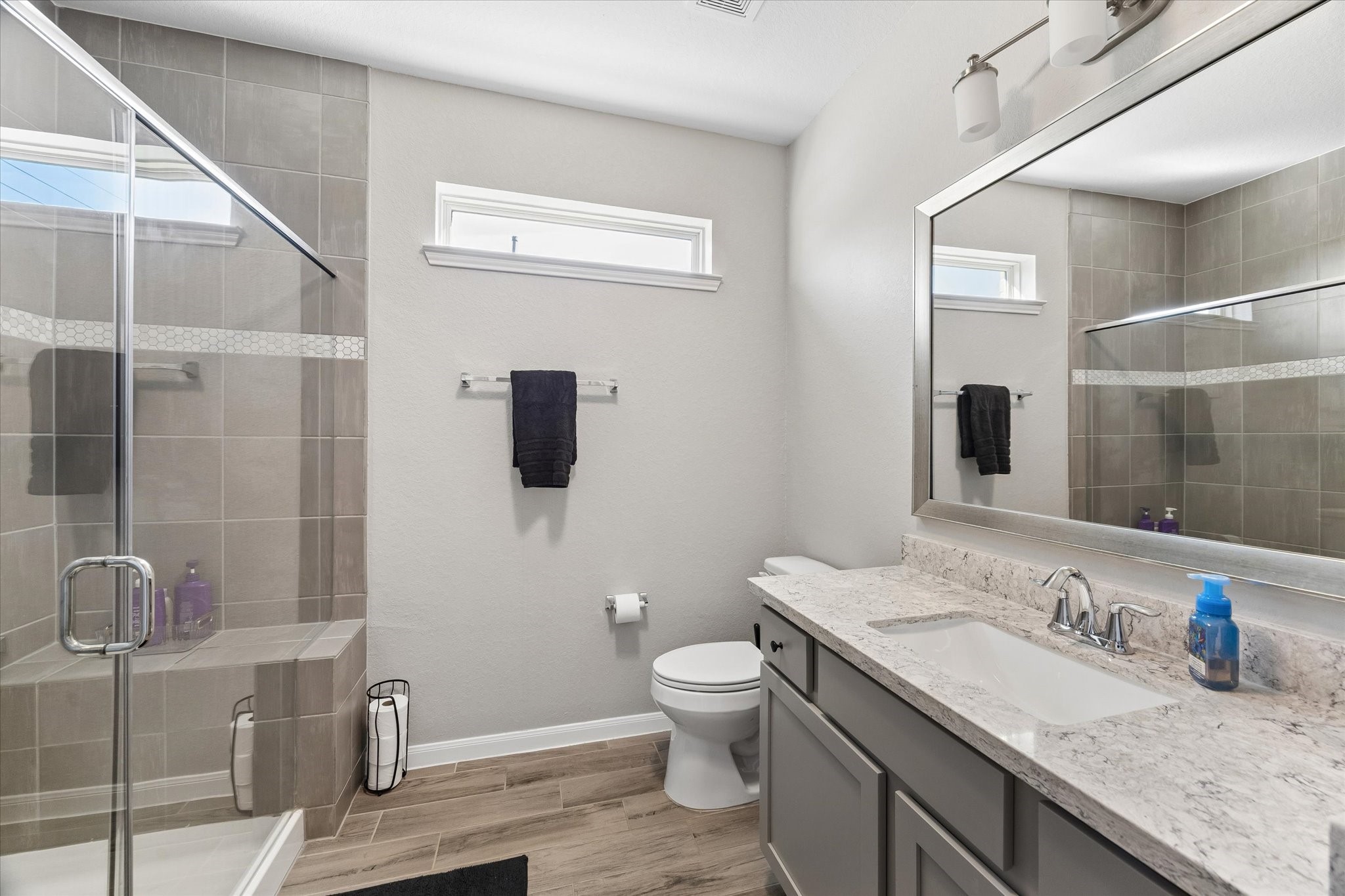 Located in the downstairs guest wing, this secondary full bathroom serves the nearby bedroom and additional living space, with a tub-and-shower combination, wide mirror, and vanity storage.