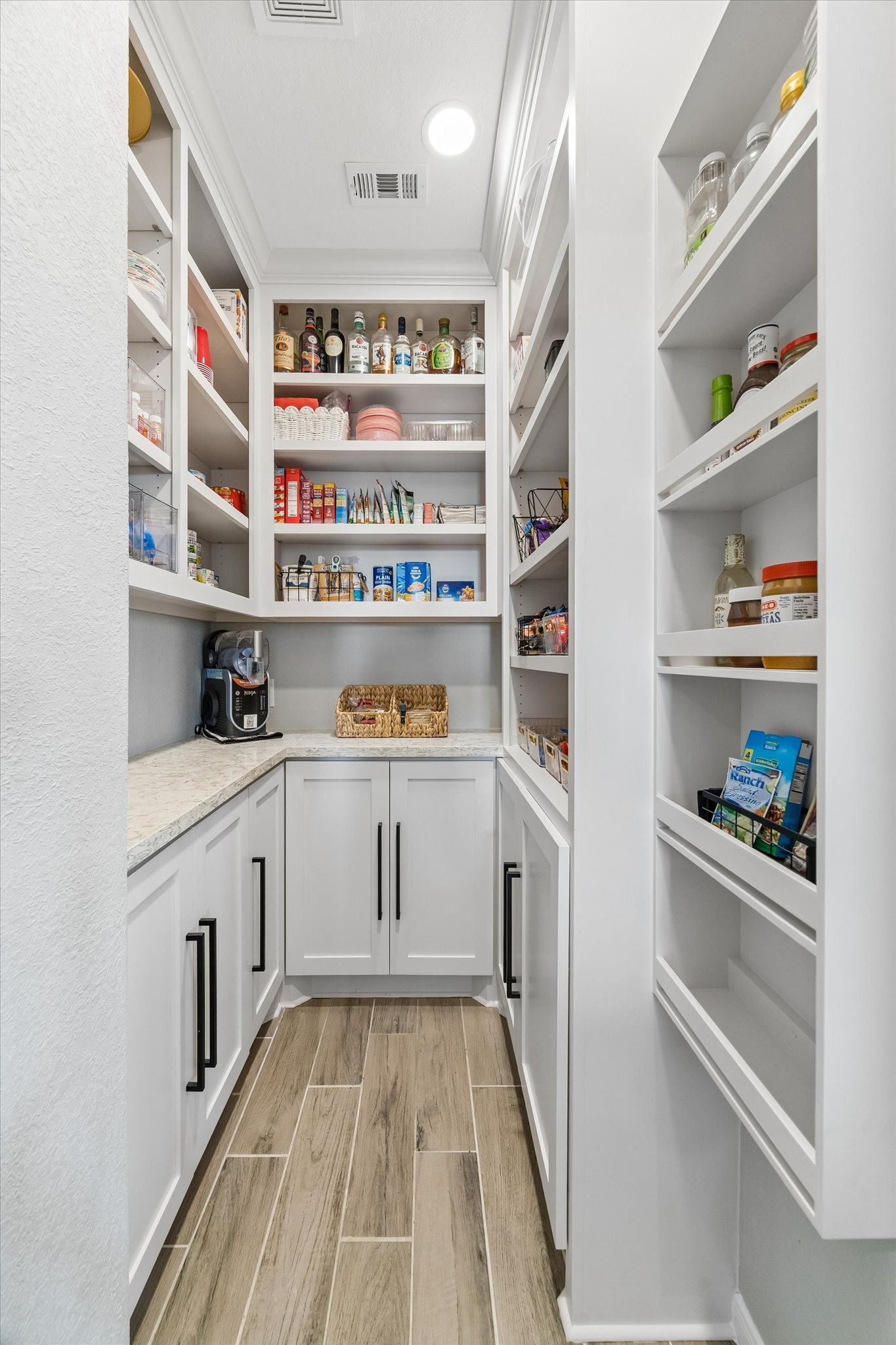 Thoughtfully redesigned in 2023, this walk-in pantry features custom cabinetry and shelving, a stone countertop for small appliances, and a built-in coffee bar with cabinets and drawers to keep everyday essentials beautifully organized.